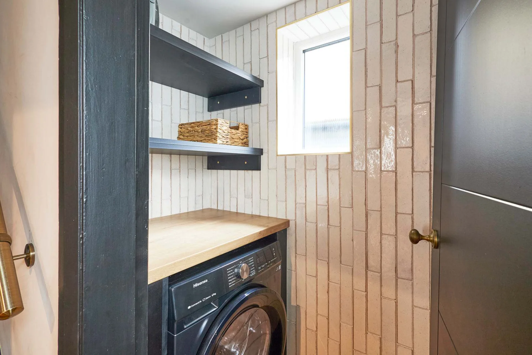 A laundry area with a washer beneath a wooden counter and open shelving.