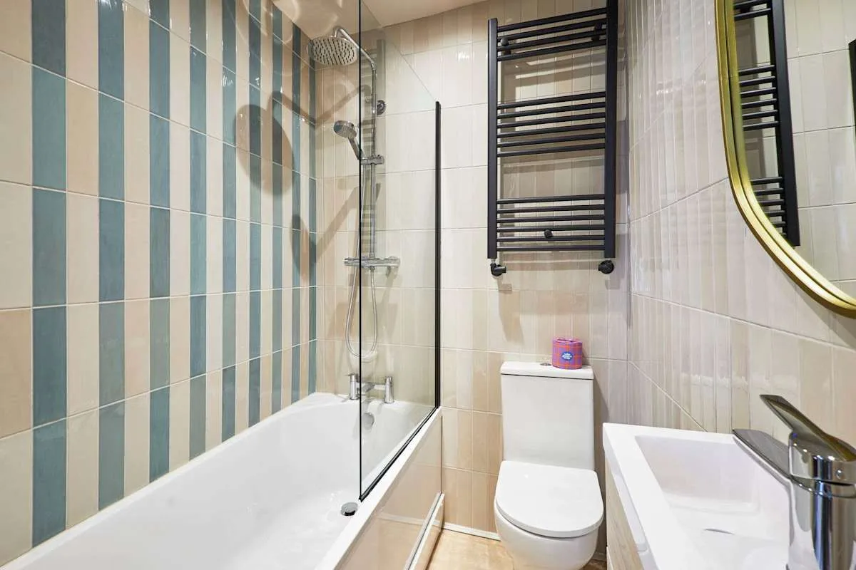 A tiled bathroom with a bathtub, toilet, and wall-mounted towel warmer.