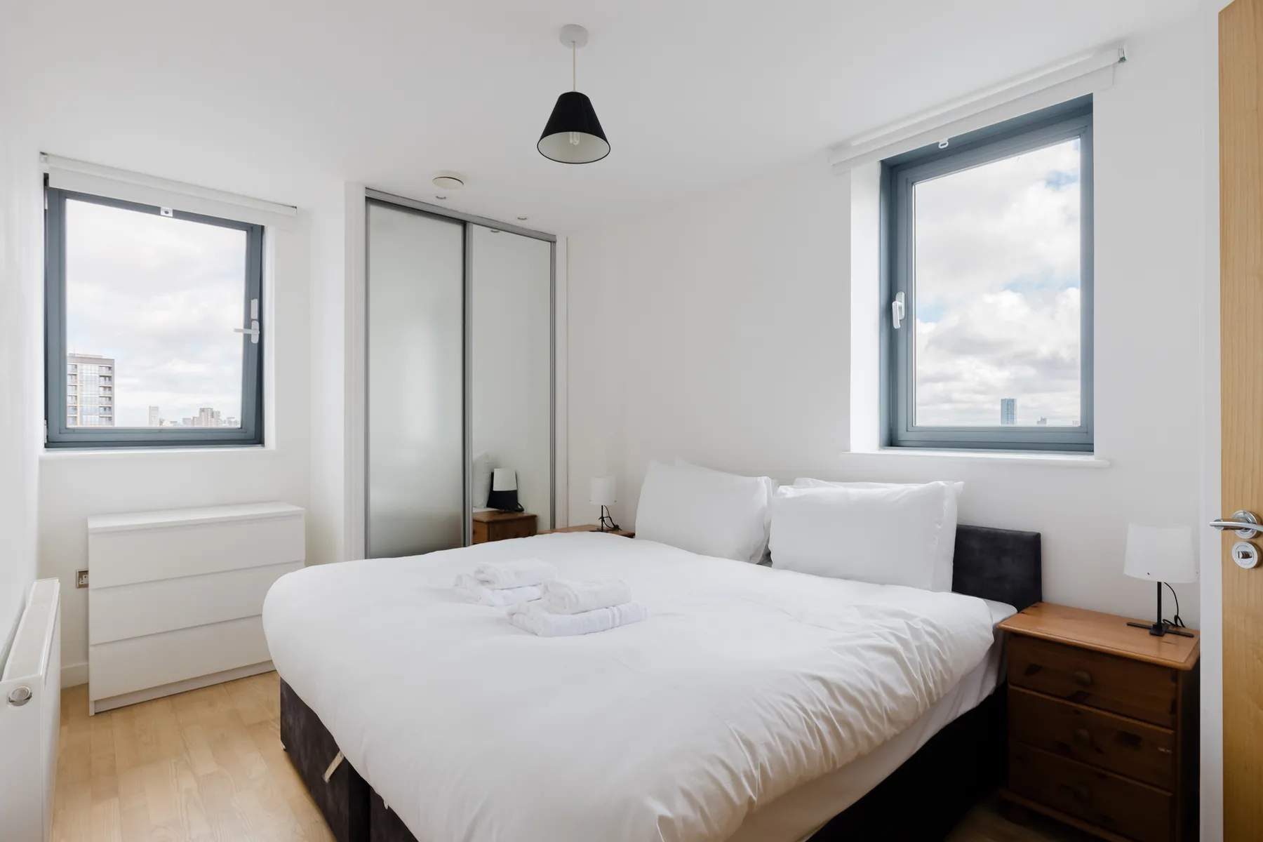 Un dormitorio luminoso con una cama tendida y dos ventanas.