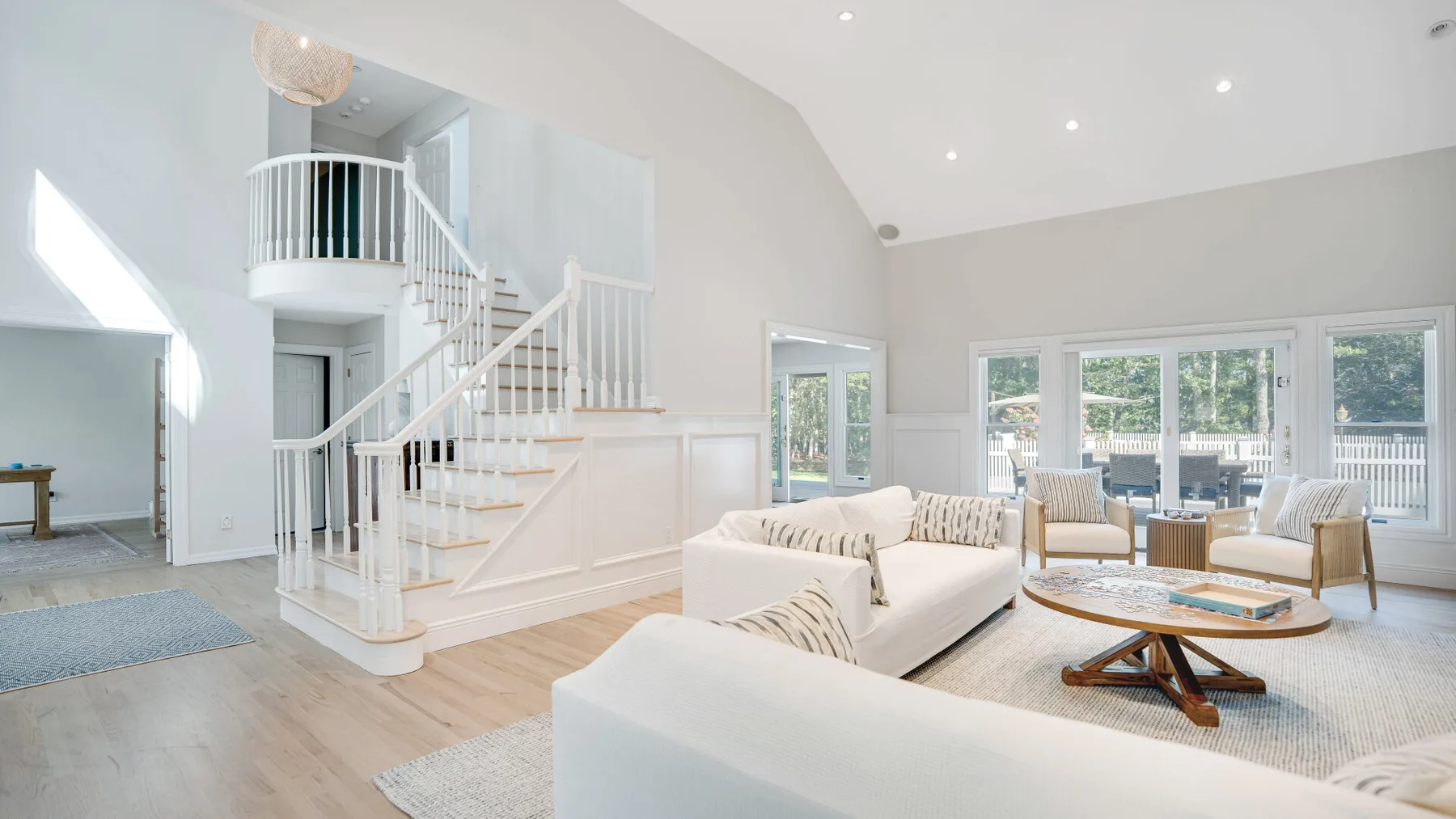 Una sala de estar luminosa con una escalera, asientos y ventanales.