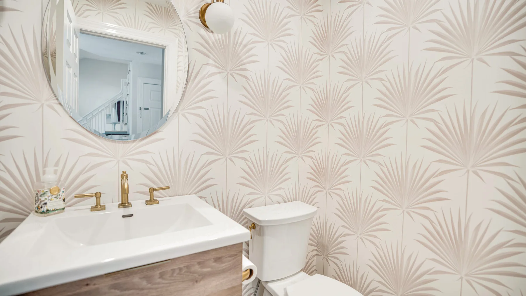 Un baño con lavabo blanco, inodoro y papel tapiz estampado.