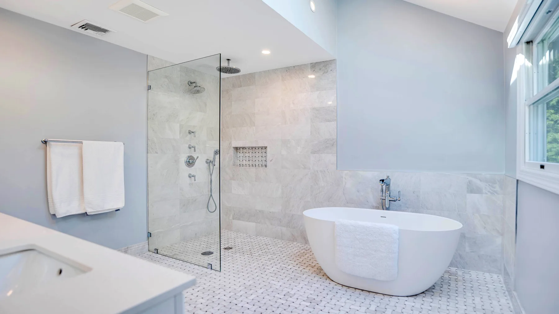 Un baño luminoso con una ducha de vidrio y una bañera independiente.