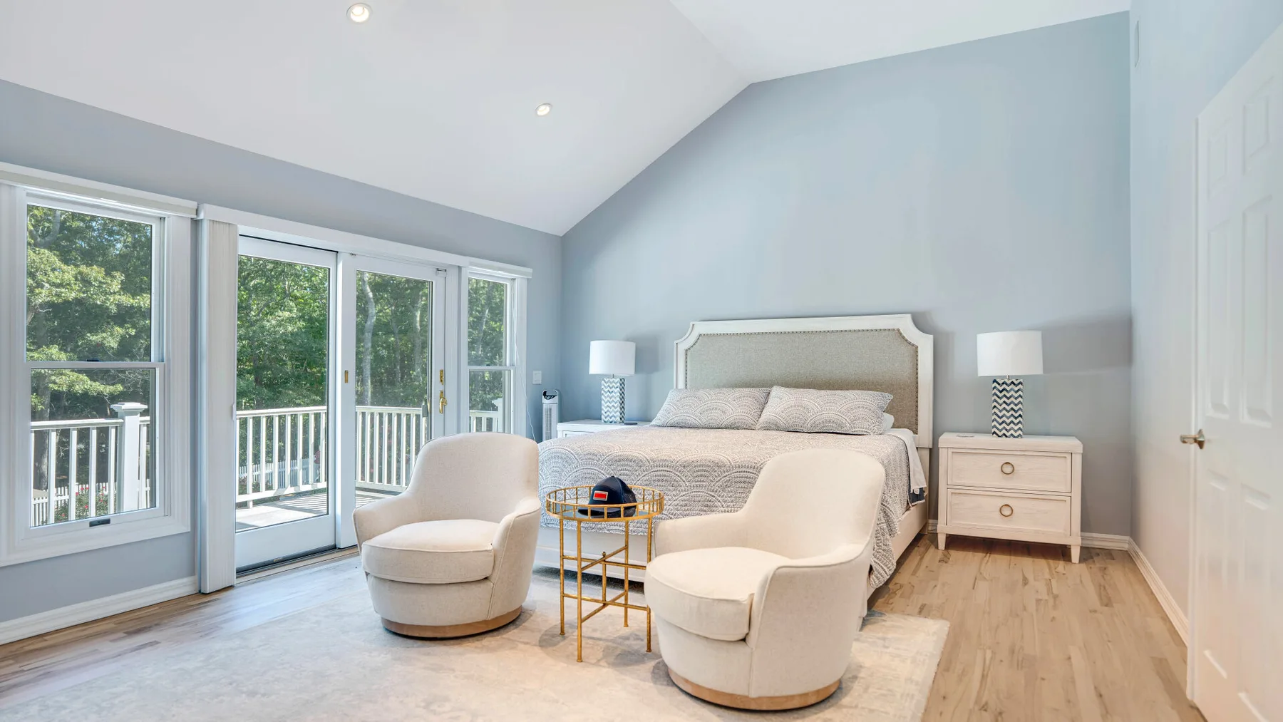 Un dormitorio luminoso con una cama, dos sillones y grandes ventanas.