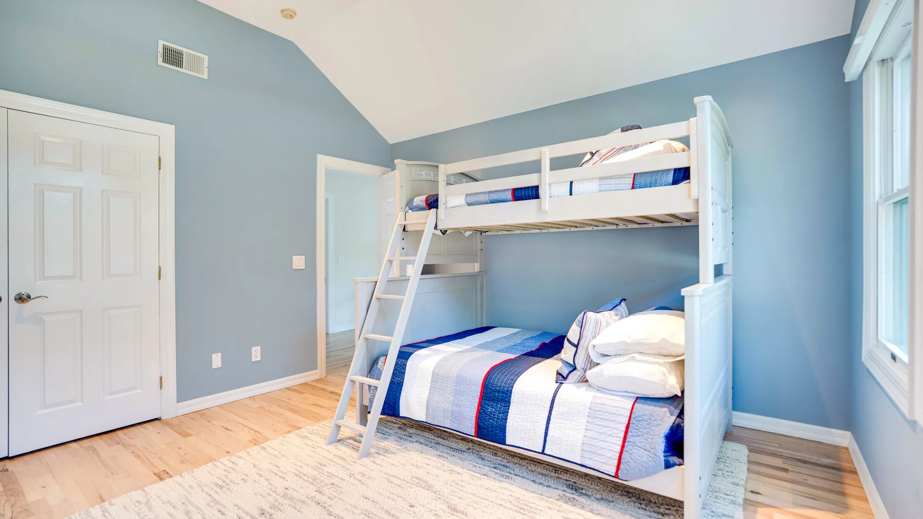 Un dormitorio luminoso con una litera blanca y ropa de cama azul y blanca.