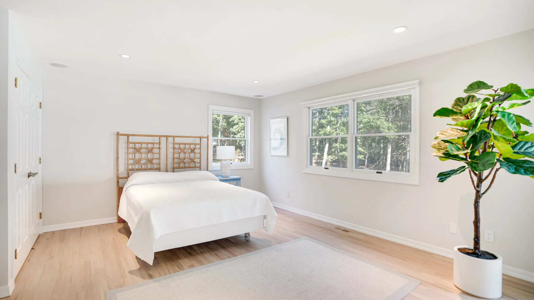 Un dormitorio luminoso con una cama, ventanas amplias y una planta en maceta.