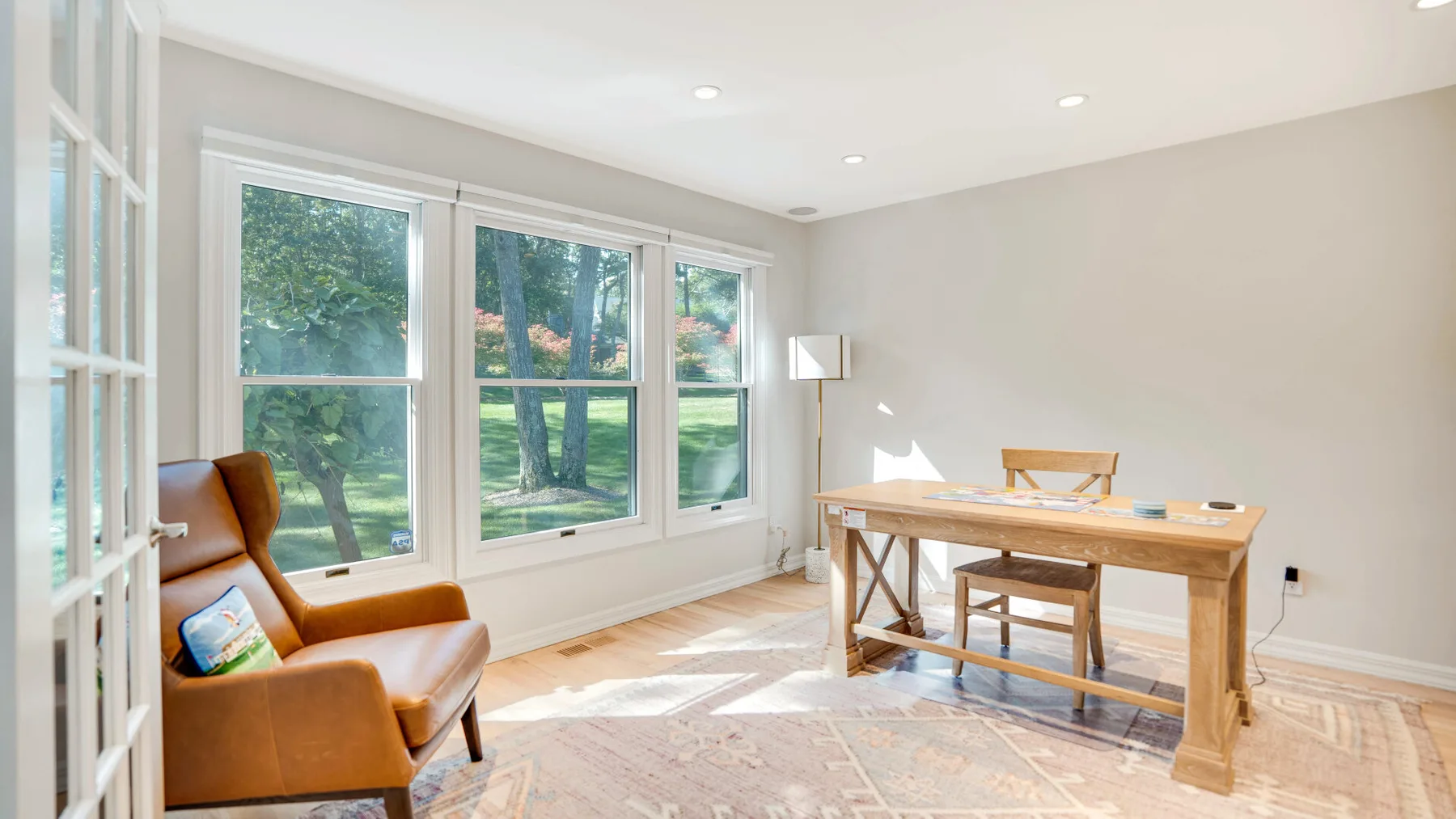 Una habitación luminosa con una mesa de madera y asientos junto a grandes ventanas.