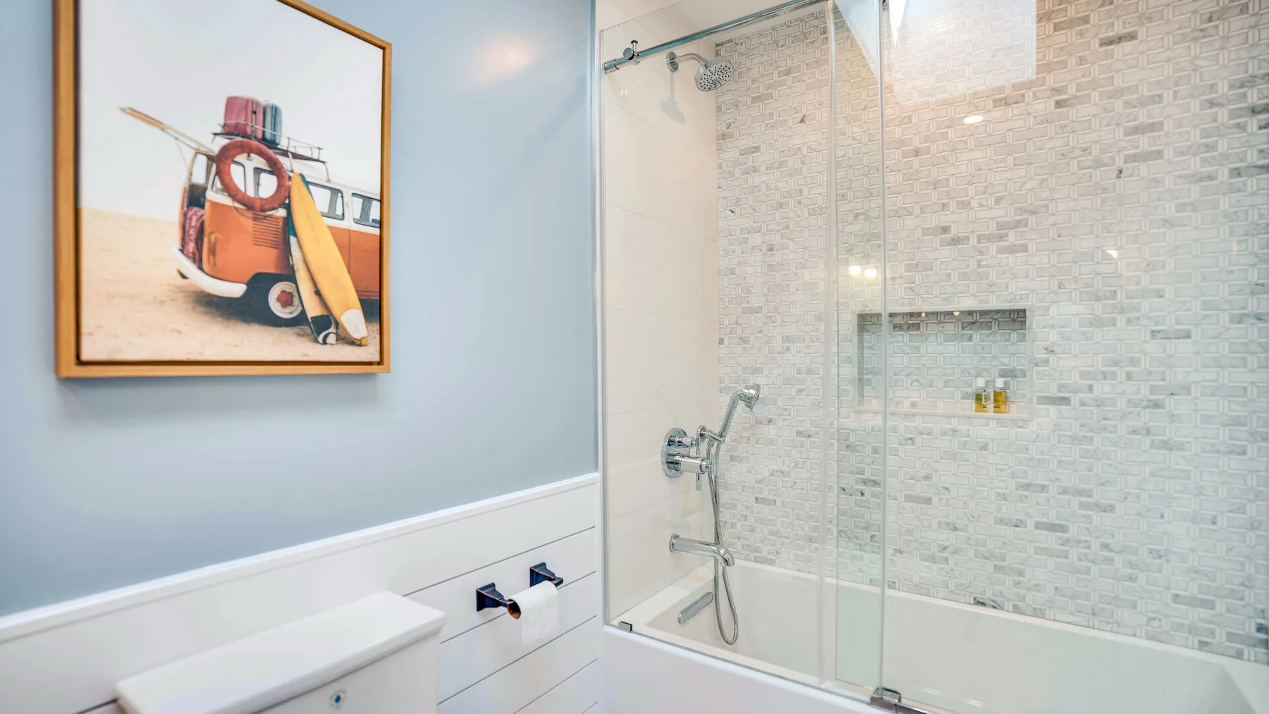 Un baño con azulejos, una ducha con mampara de vidrio y un cuadro enmarcado.
