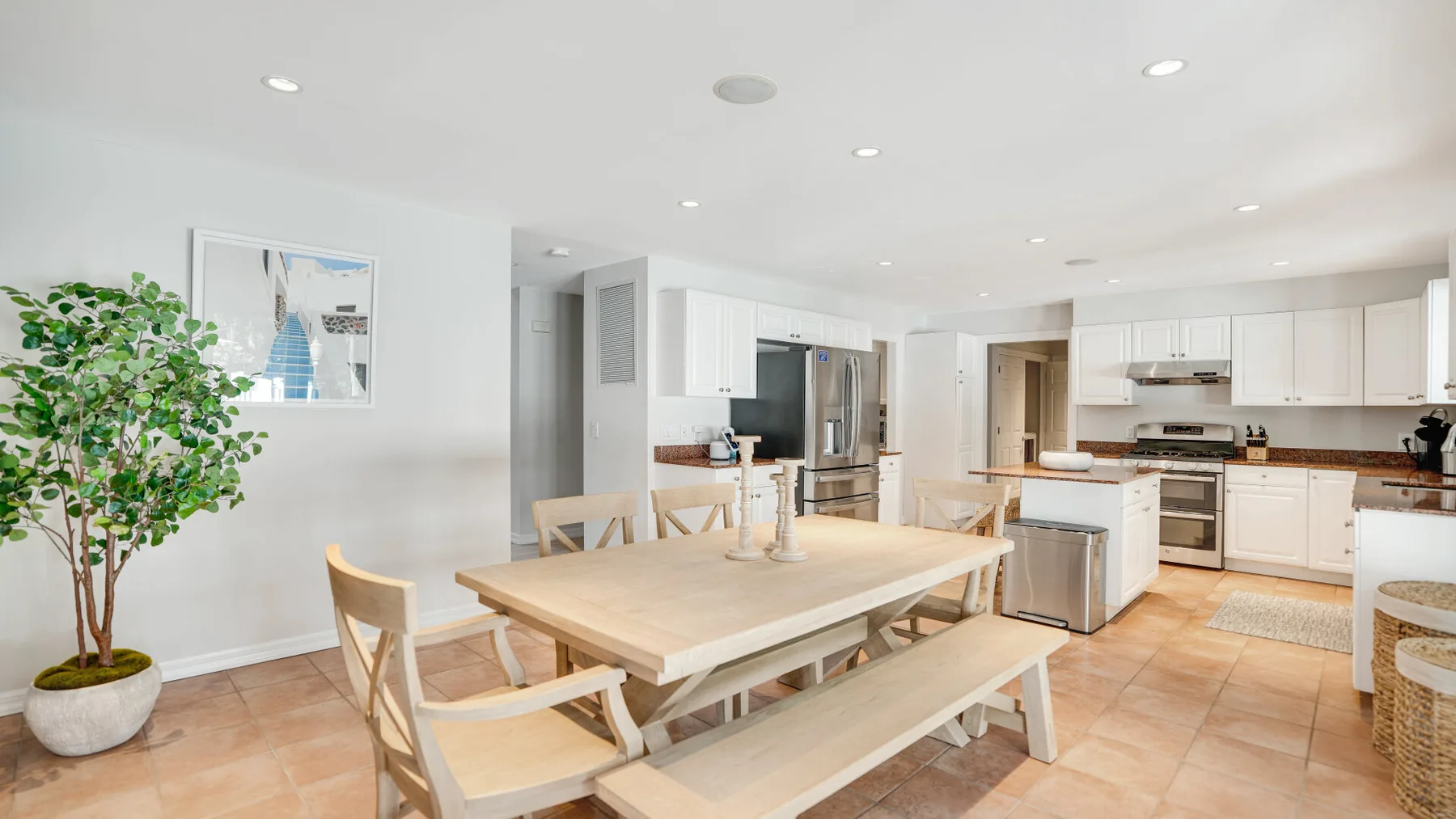 Una cocina y zona de comedor luminosa con una mesa de madera y armarios blancos.