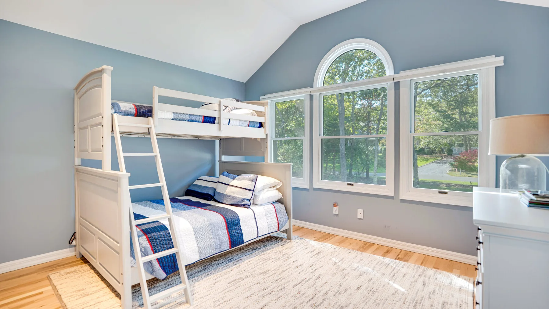 Un dormitorio luminoso con literas y grandes ventanas con vistas a los árboles.