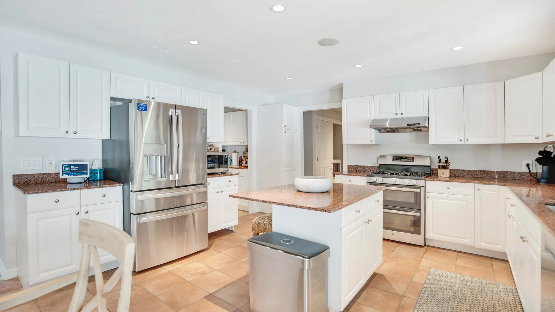 Una cocina luminosa con gabinetes blancos, electrodomésticos de acero inoxidable y una isla central.