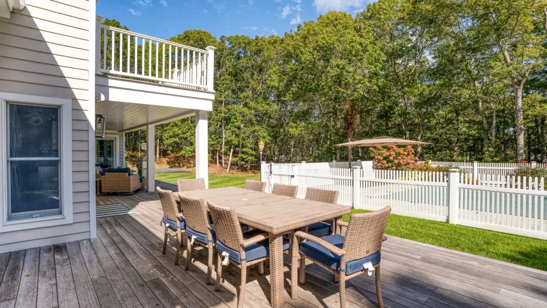 Una terraza de madera junto a la casa tiene una mesa de comedor y asientos al aire libre.