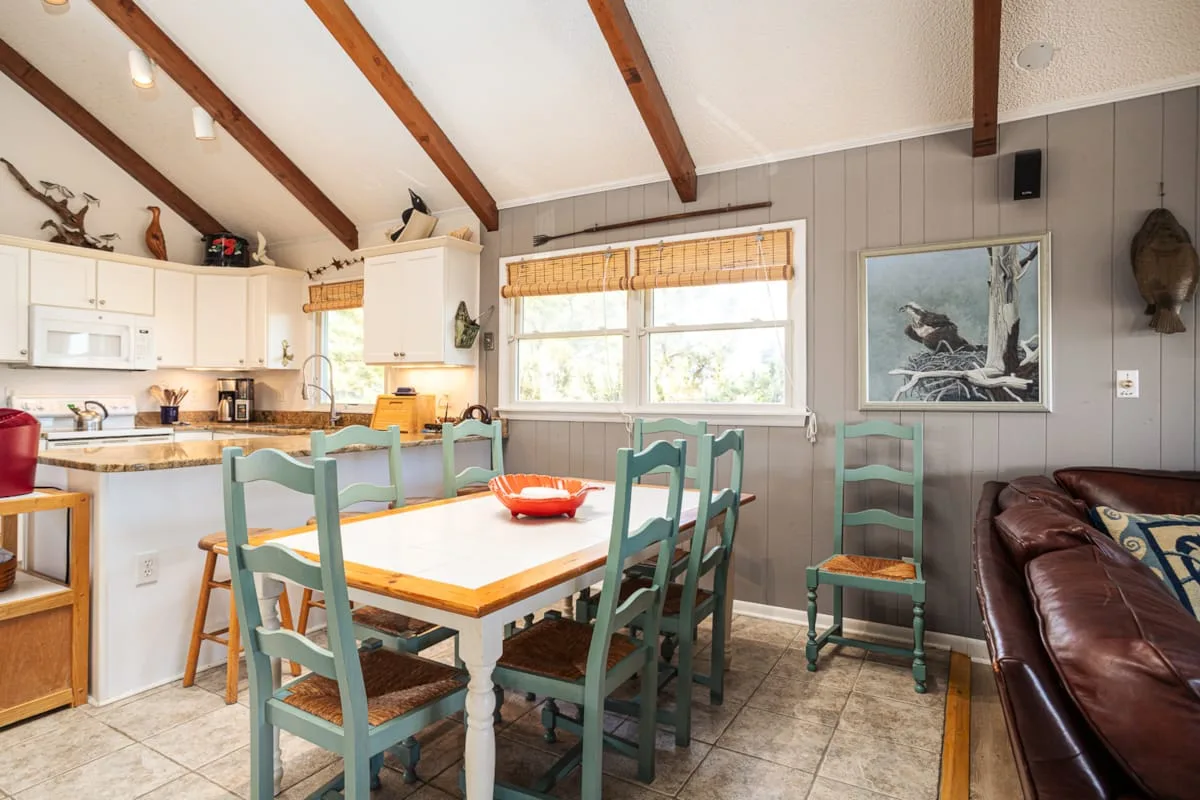 Un comedor con una mesa de madera y sillas verdes junto a una cocina abierta.