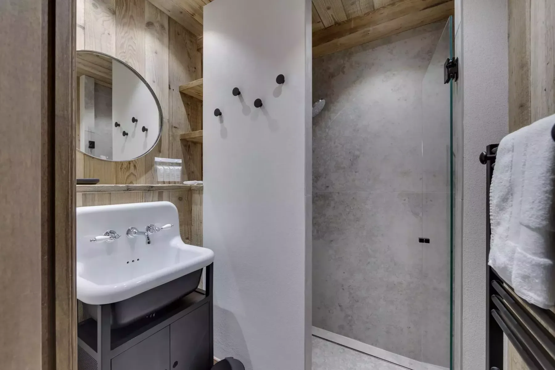 A bathroom with a sink, wall hooks, and a glass shower screen.