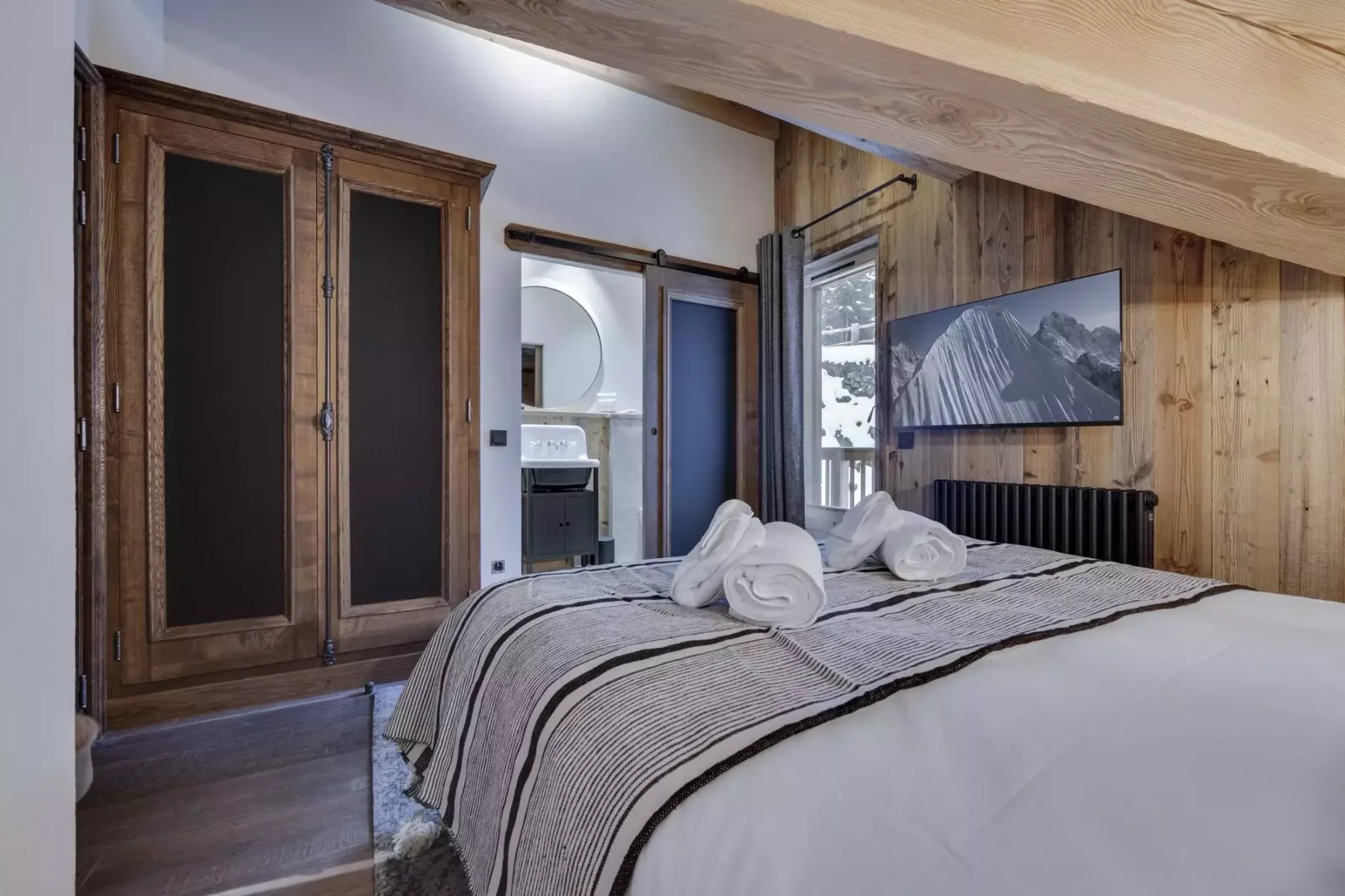 A bedroom with a neatly made bed and a wooden wardrobe.