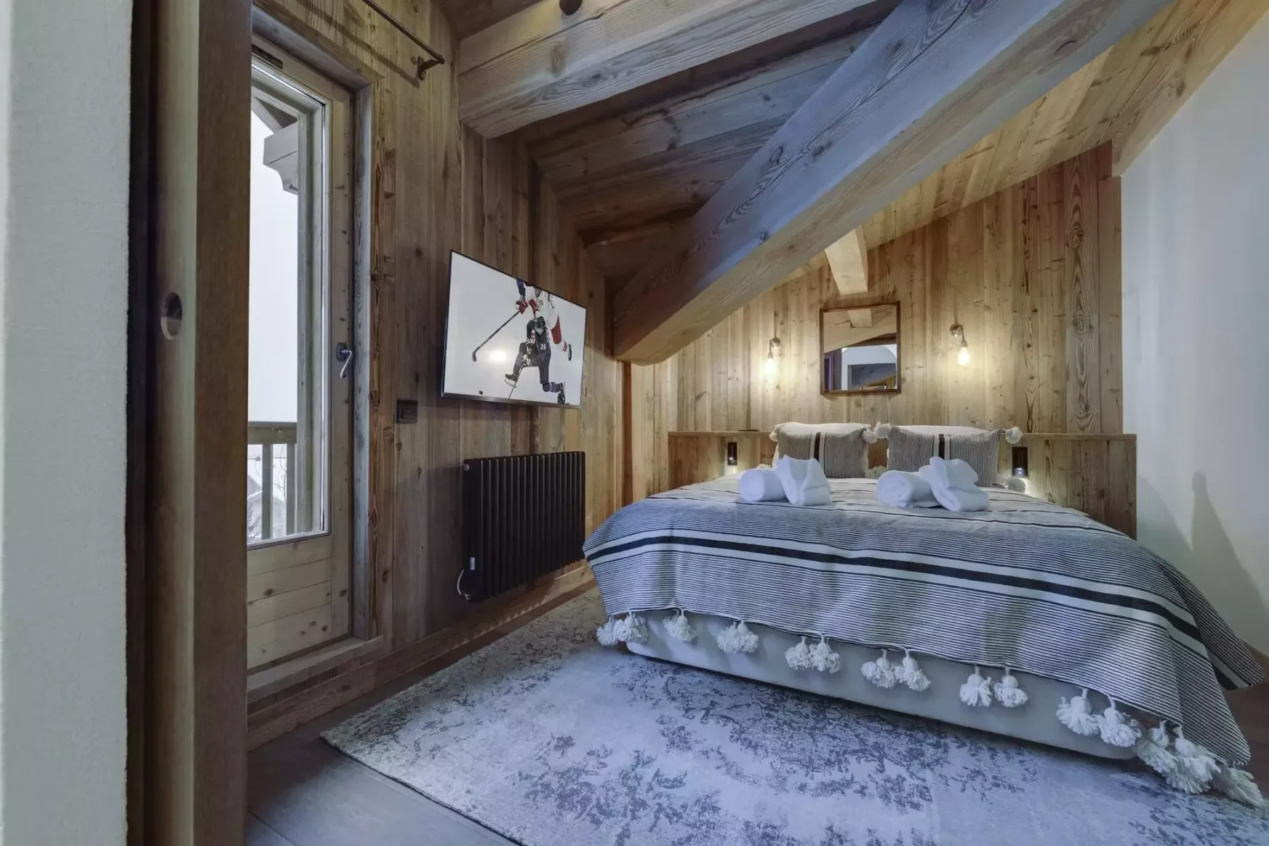 A wood-paneled bedroom with a neatly made bed beneath a sloped ceiling.