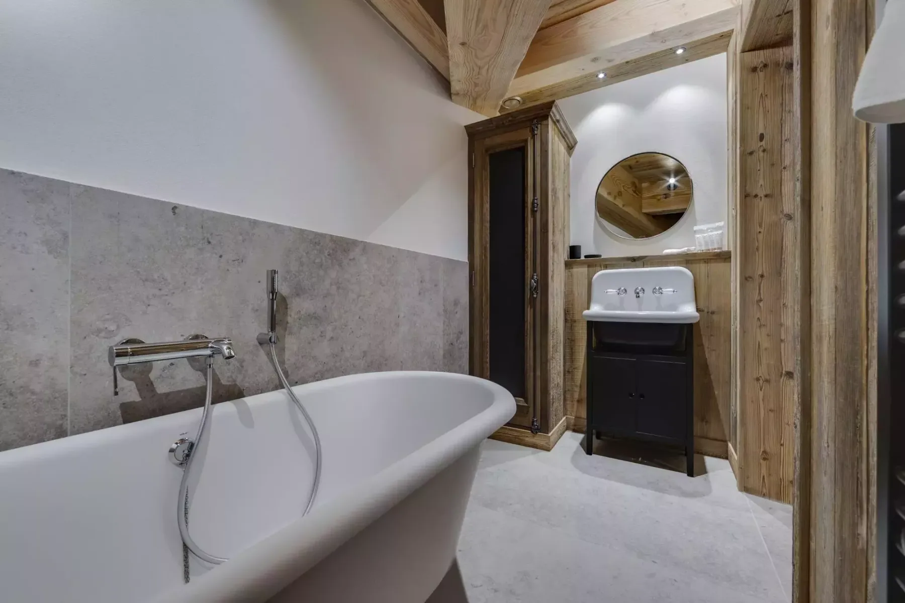 A bathroom with a freestanding bathtub, sink, and round mirror.