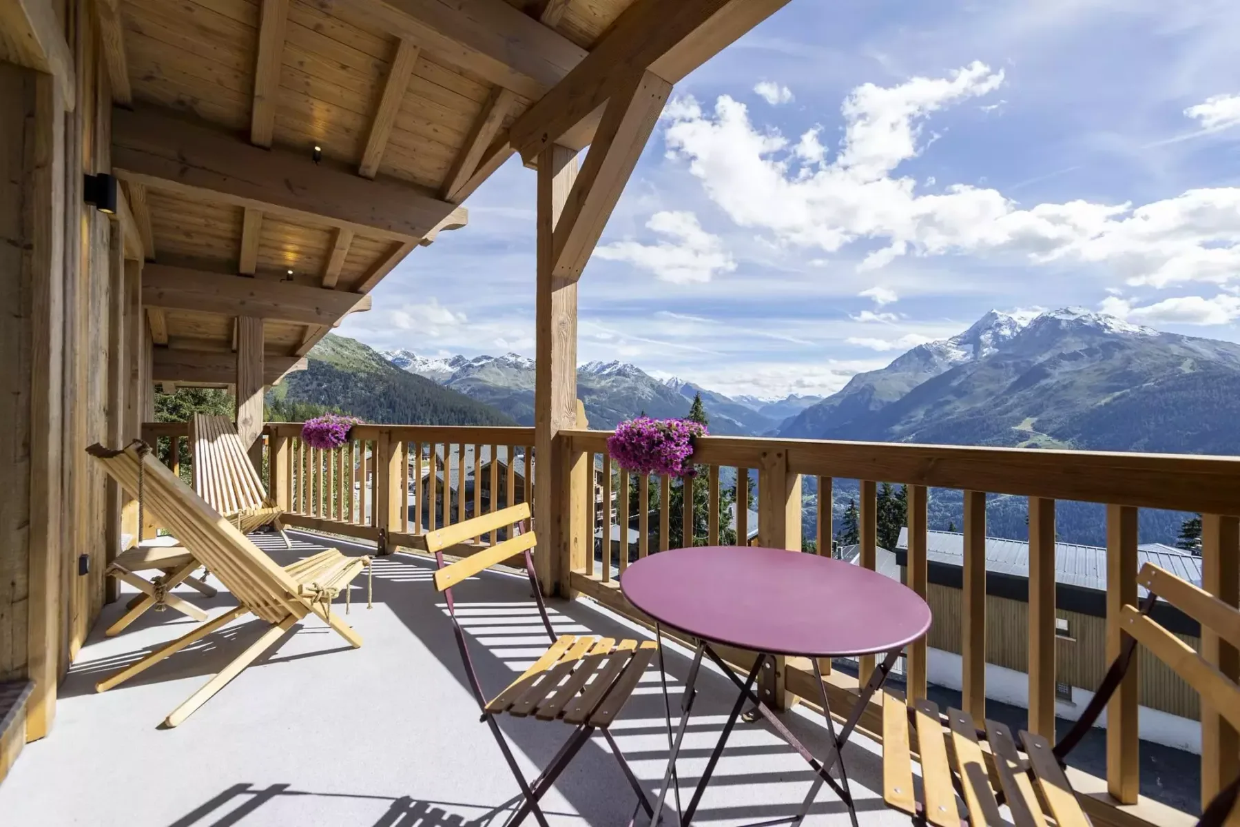 A covered wooden terrace with outdoor seating overlooks a mountain landscape.