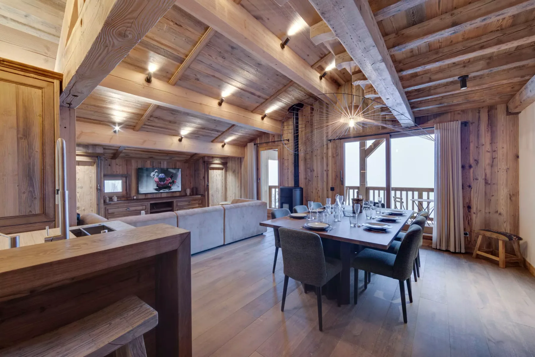 A wood-paneled living and dining room with a long table beside large windows.