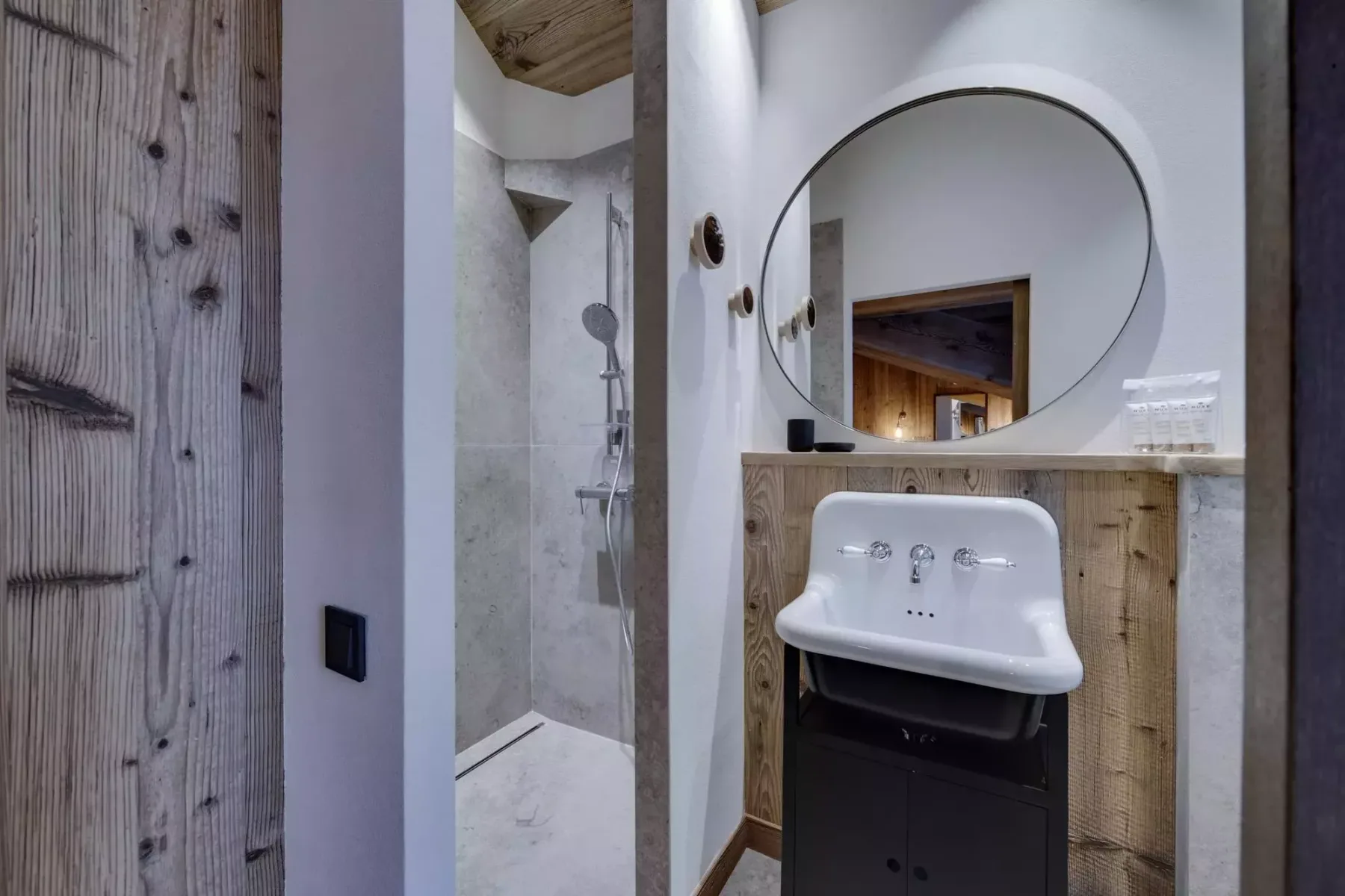 A bathroom with a wall-mounted sink and round mirror beside a shower.