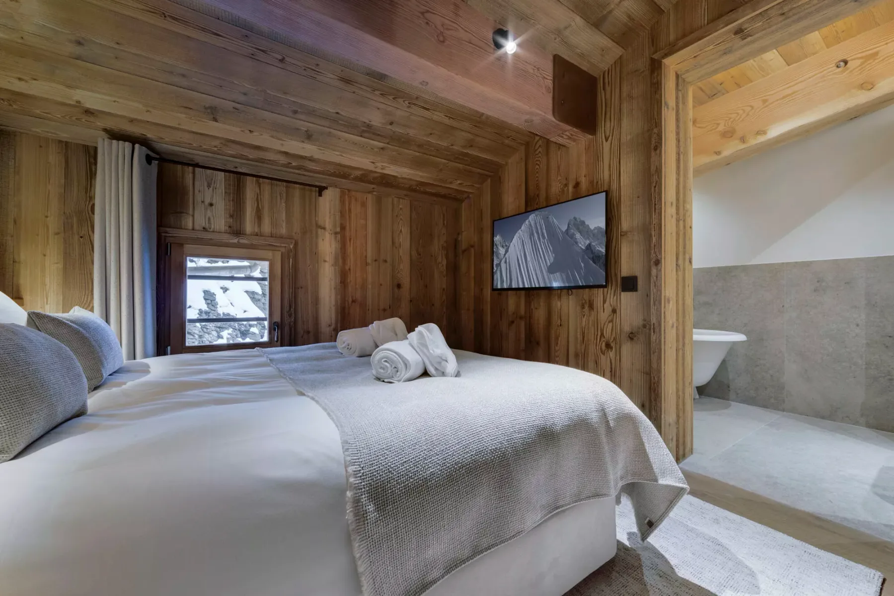 A wood-paneled bedroom with beds, a wall-mounted television, and an adjoining bathroom.