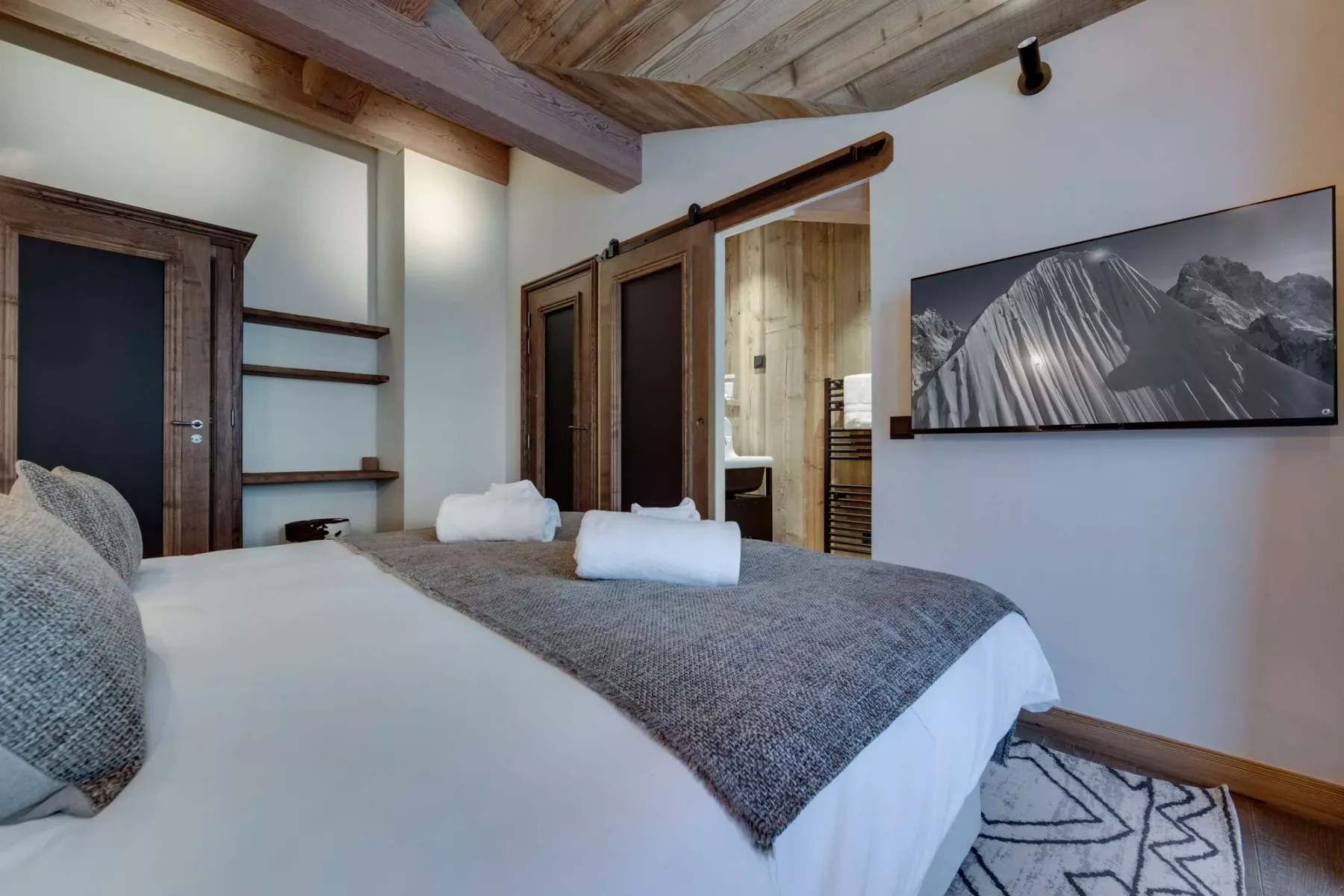 A bedroom with a neatly made bed and a mountain photograph on the wall.