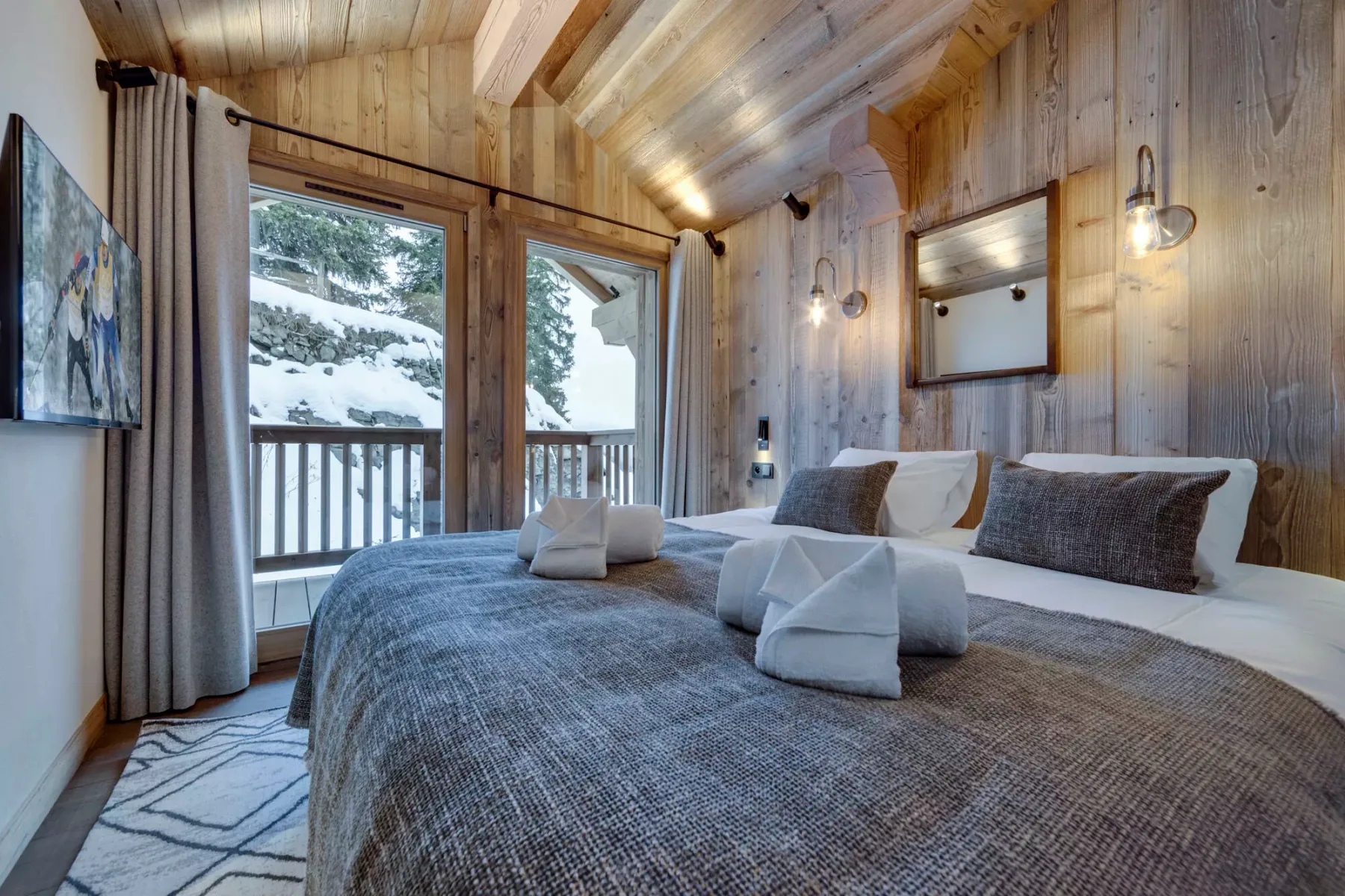 A wood-paneled bedroom with two beds and windows overlooking a snowy landscape.