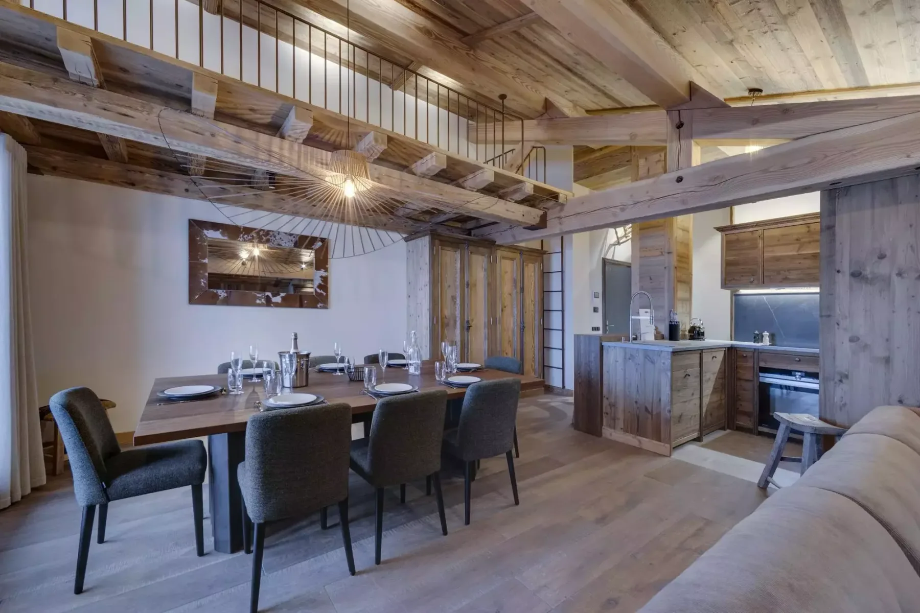 A dining and kitchen area sits beneath a wooden loft, with a table and seating.