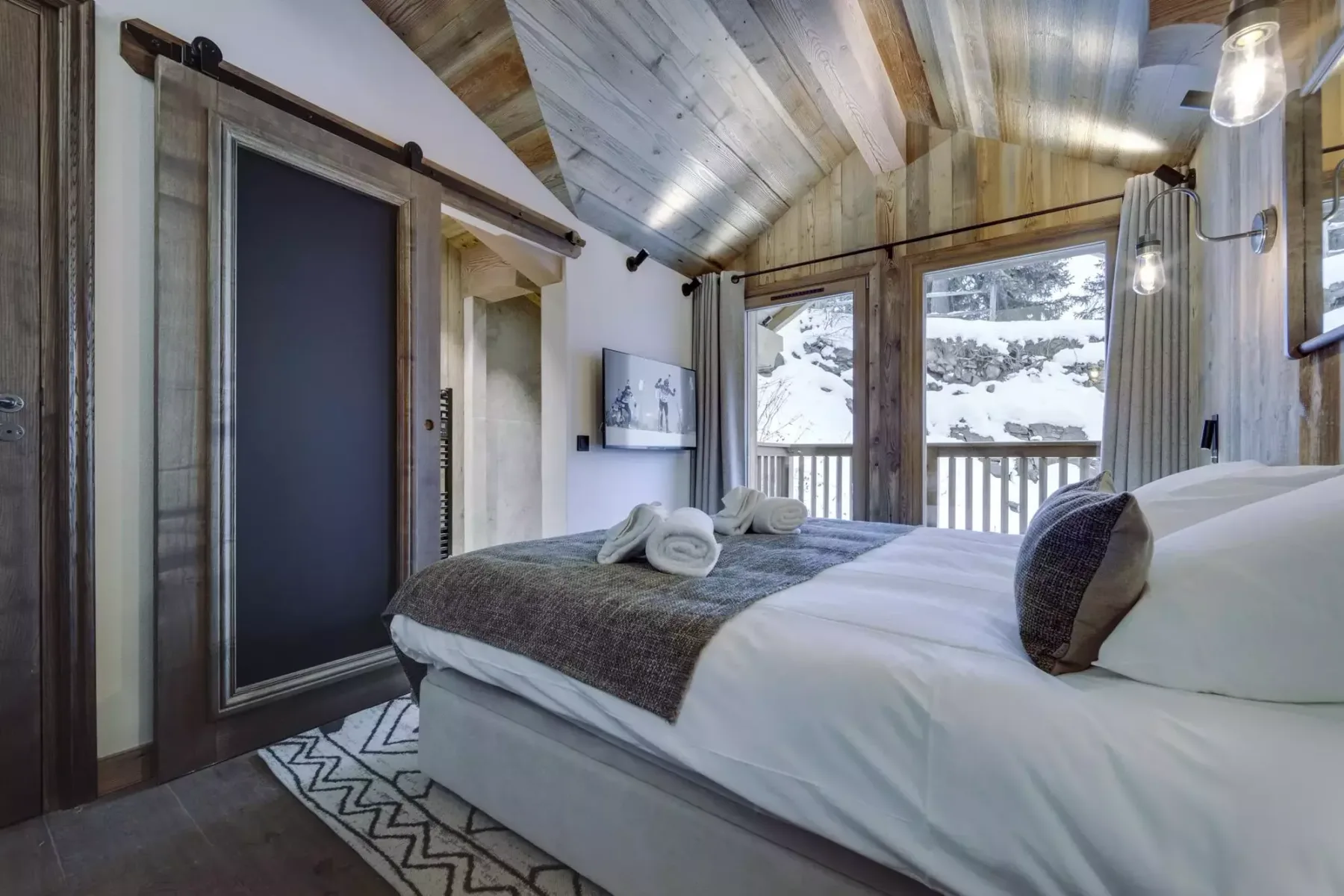 A bedroom with a neatly made bed and large windows overlooking a snowy landscape.