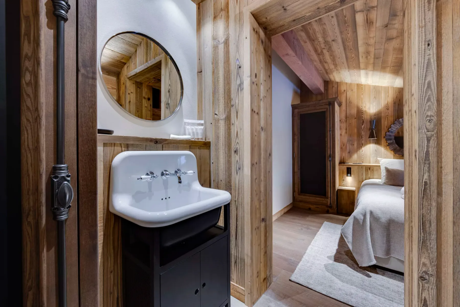 A wood-paneled bathroom vanity opens onto a bedroom with a bed and rug.