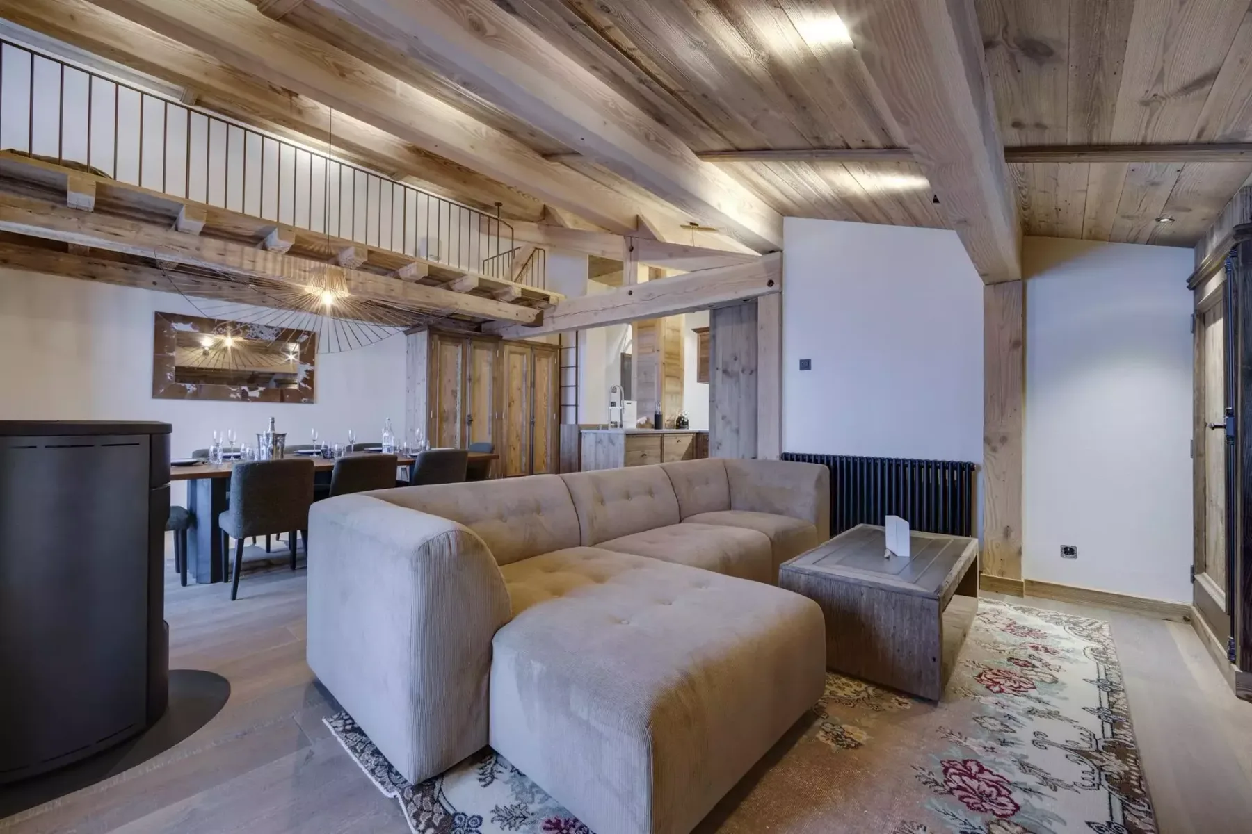 A living room with a sectional sofa and dining area beneath a wooden ceiling.