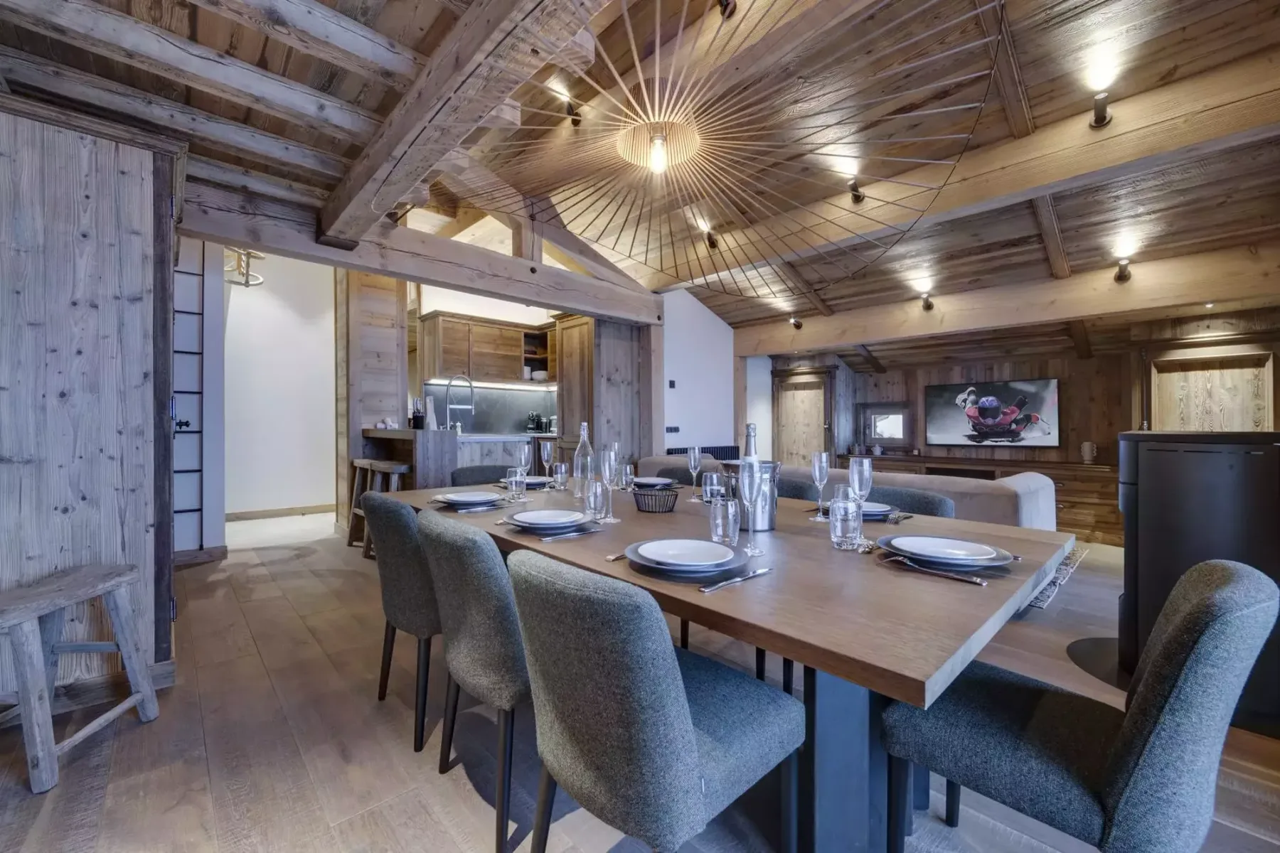 A dining area with a long table set with plates beneath a wood-beamed ceiling.