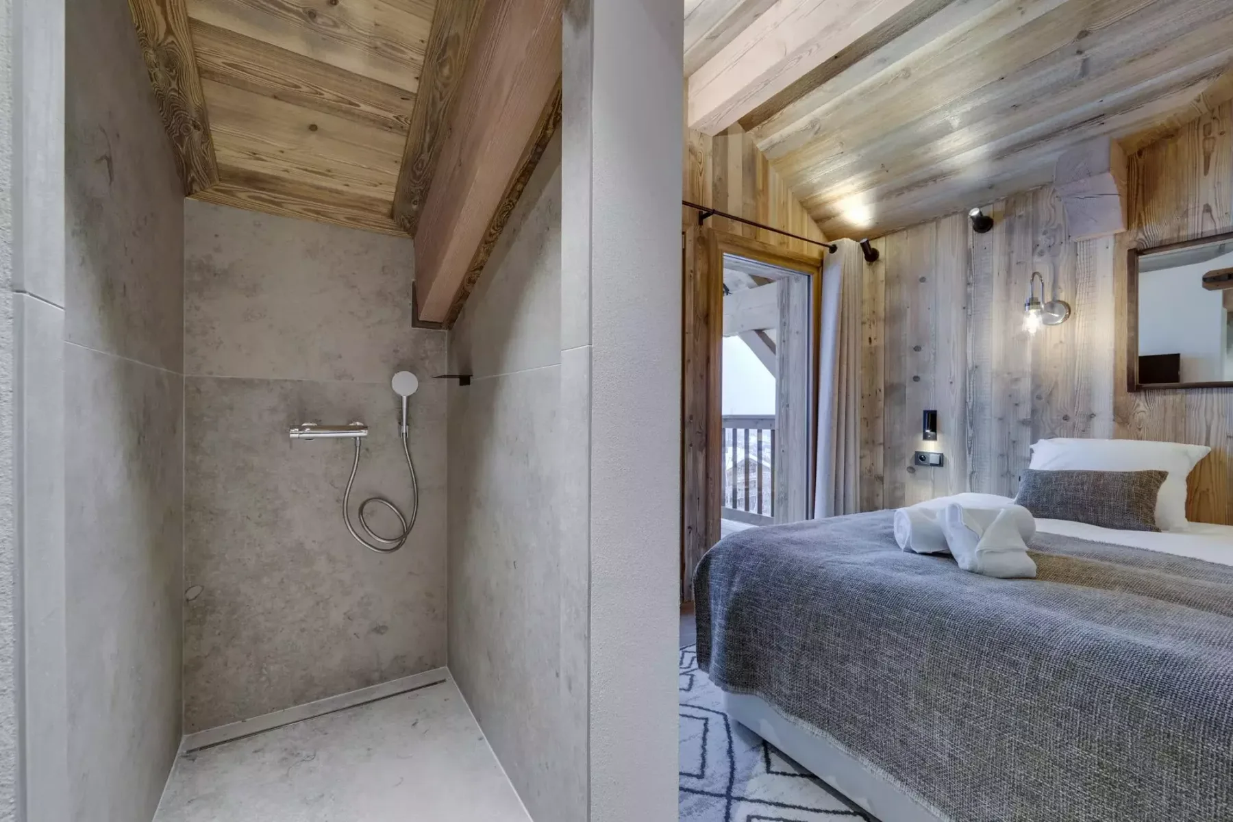 A bedroom with a neatly made bed beside a stone shower.