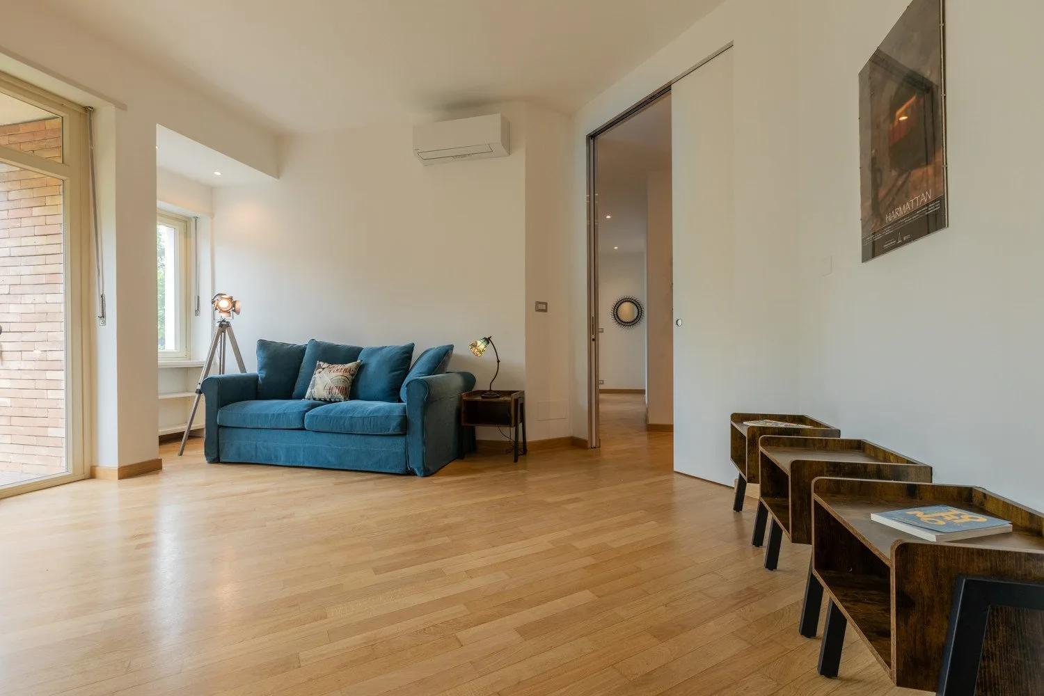A living room with blue seating, a wooden floor, and a row of small tables.