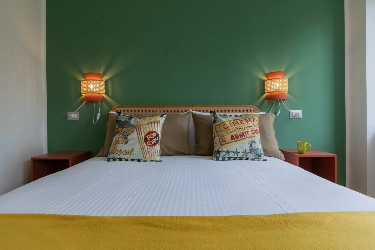 A bedroom with a neatly made bed against a green wall.
