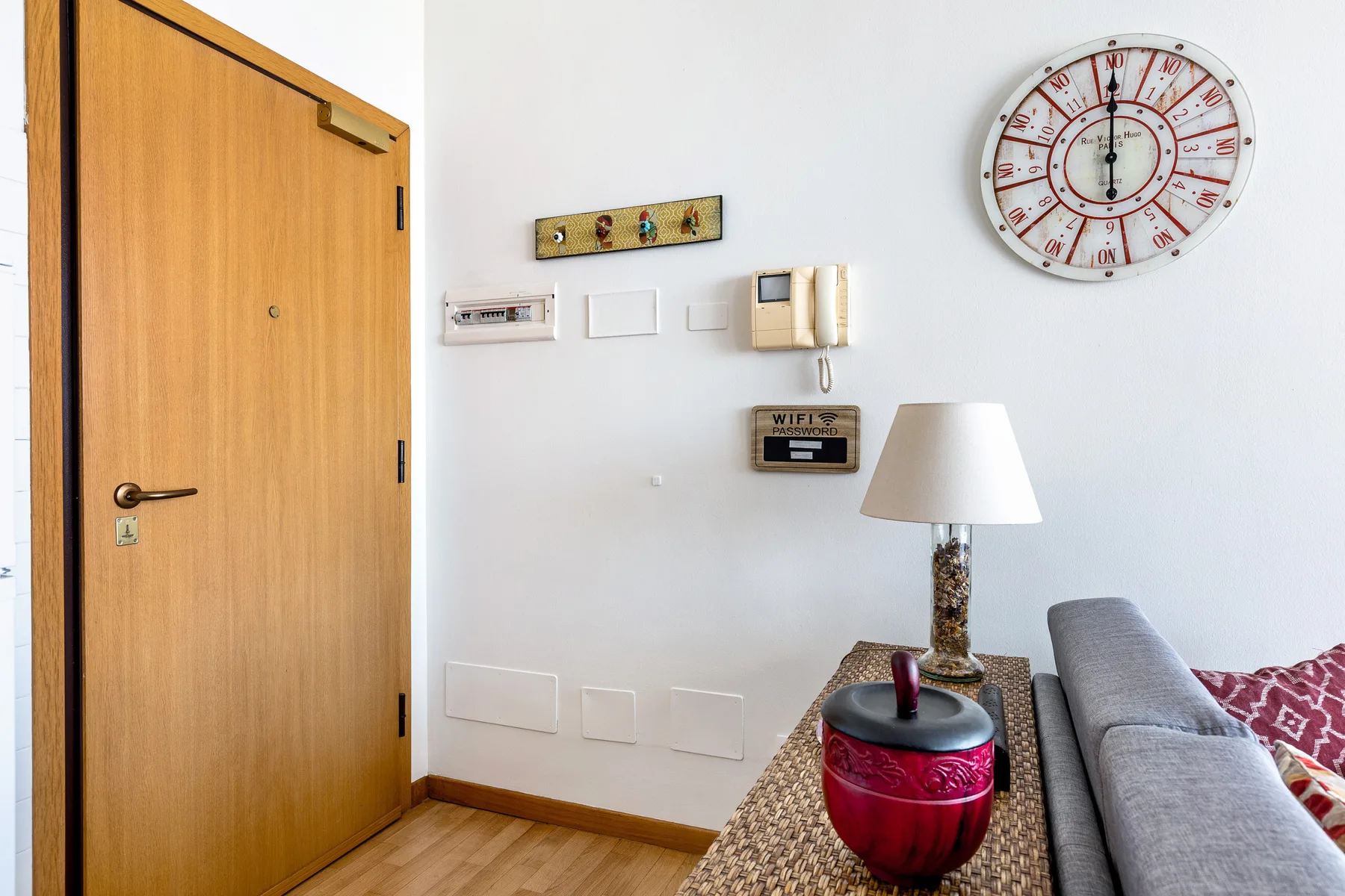 Una sala de estar con sofá gris, mesa estampada y reloj de pared.