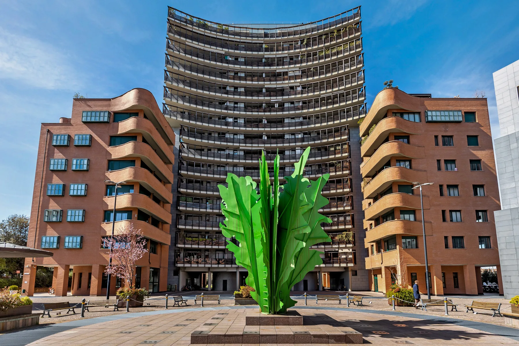 Una gran escultura verde se alza en una plaza pavimentada frente a varios edificios de oficinas.