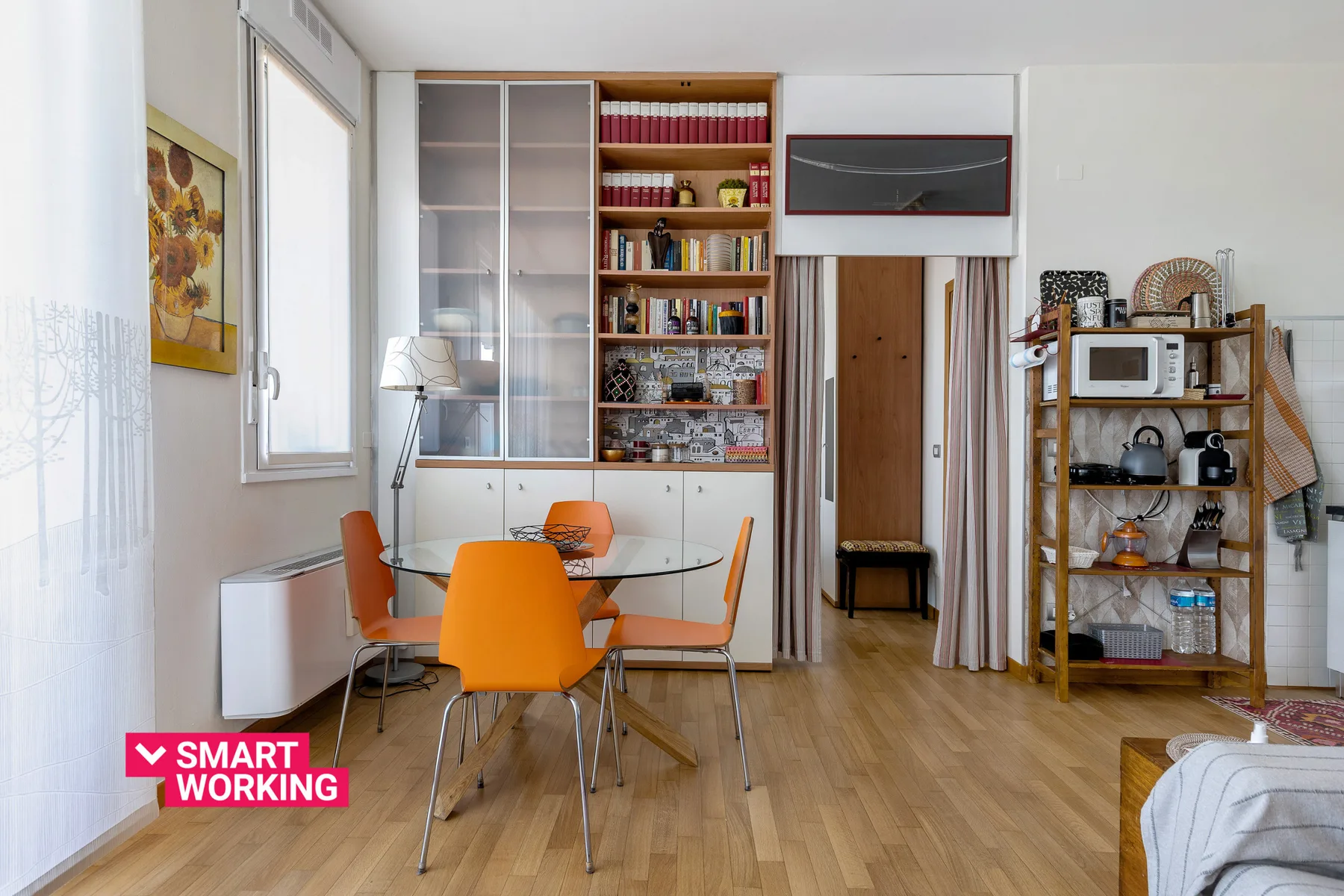 Un comedor luminoso con asientos naranjas, una mesa de vidrio y estanterías empotradas.