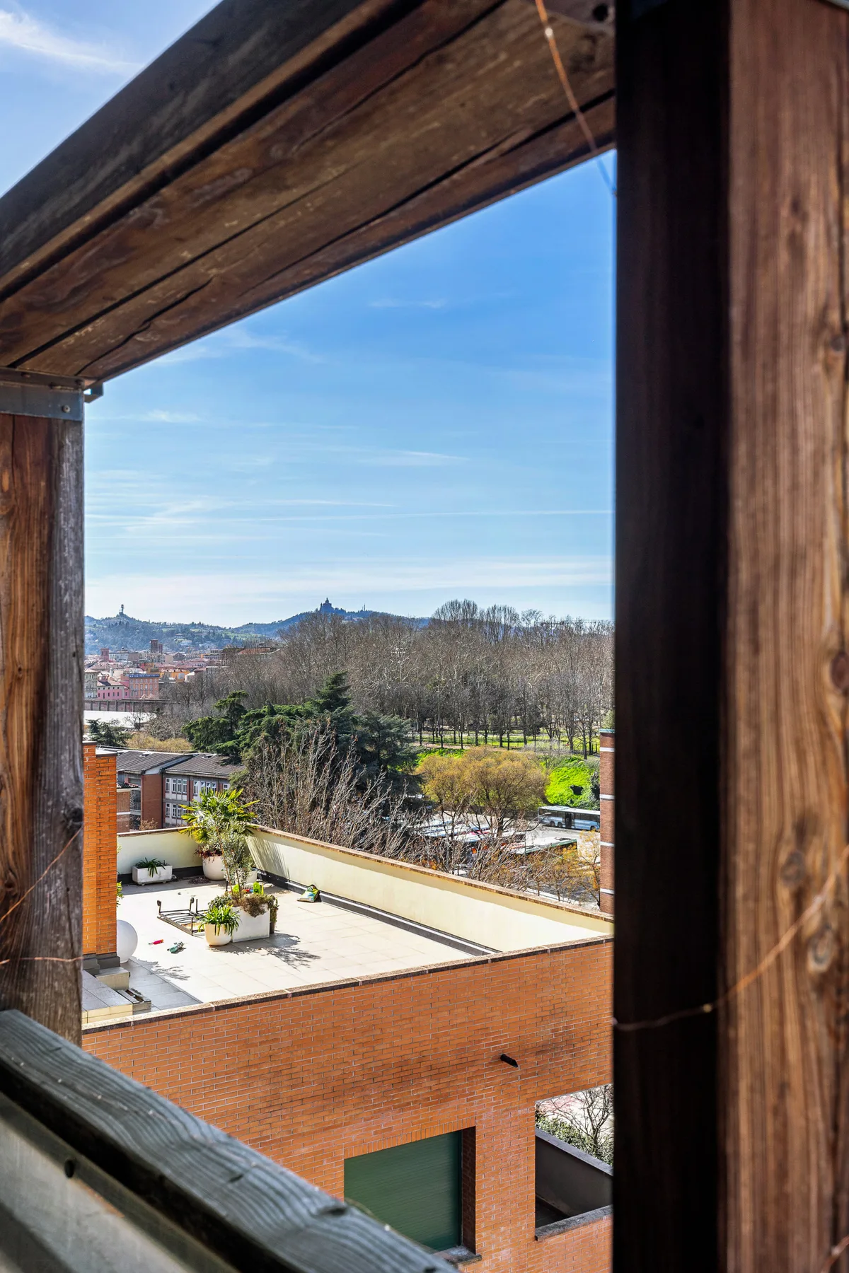 Una terraza en la azotea y árboles cercanos se ven a través de una abertura con marco de madera.