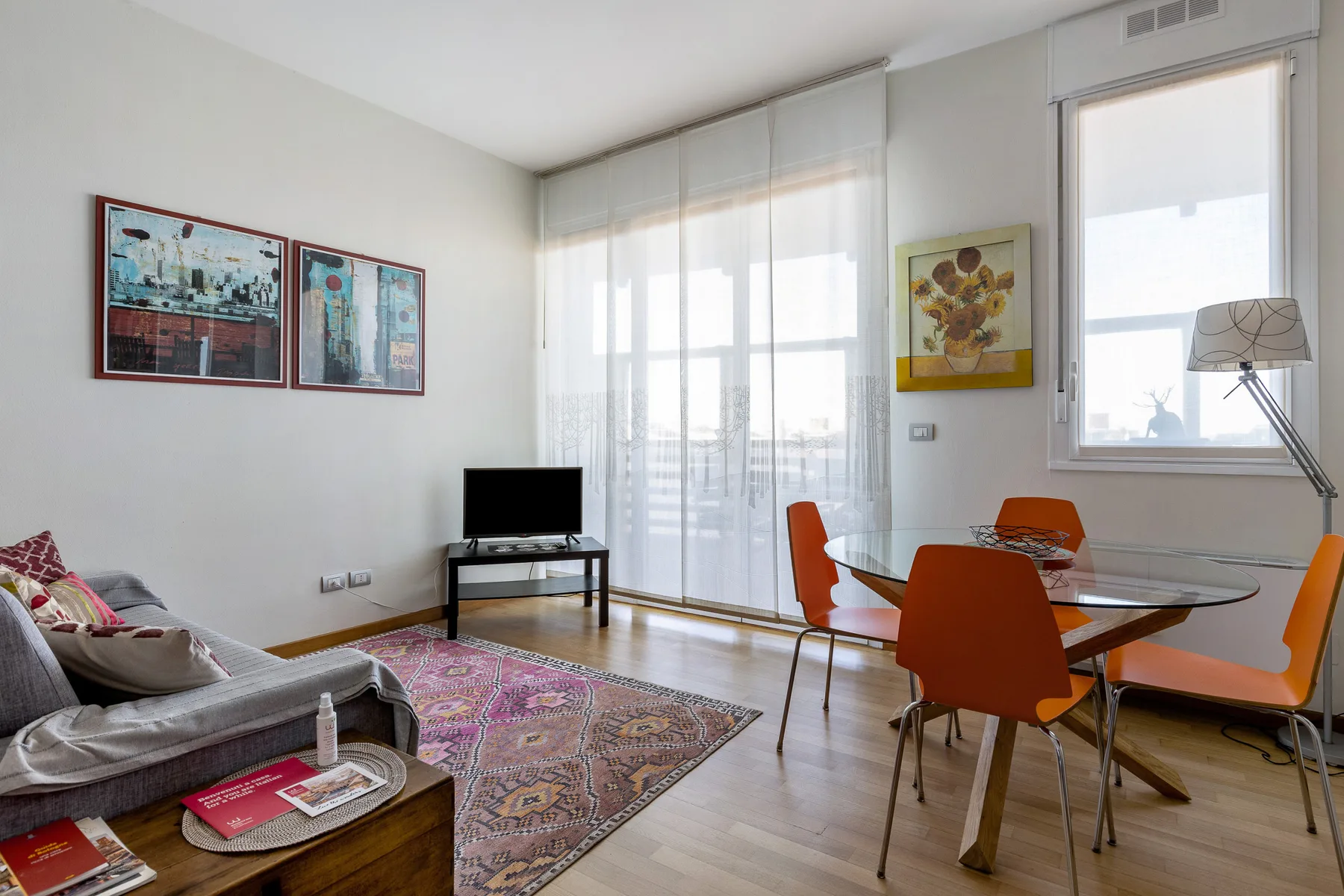 Un salón-comedor luminoso con una alfombra y grandes ventanas.