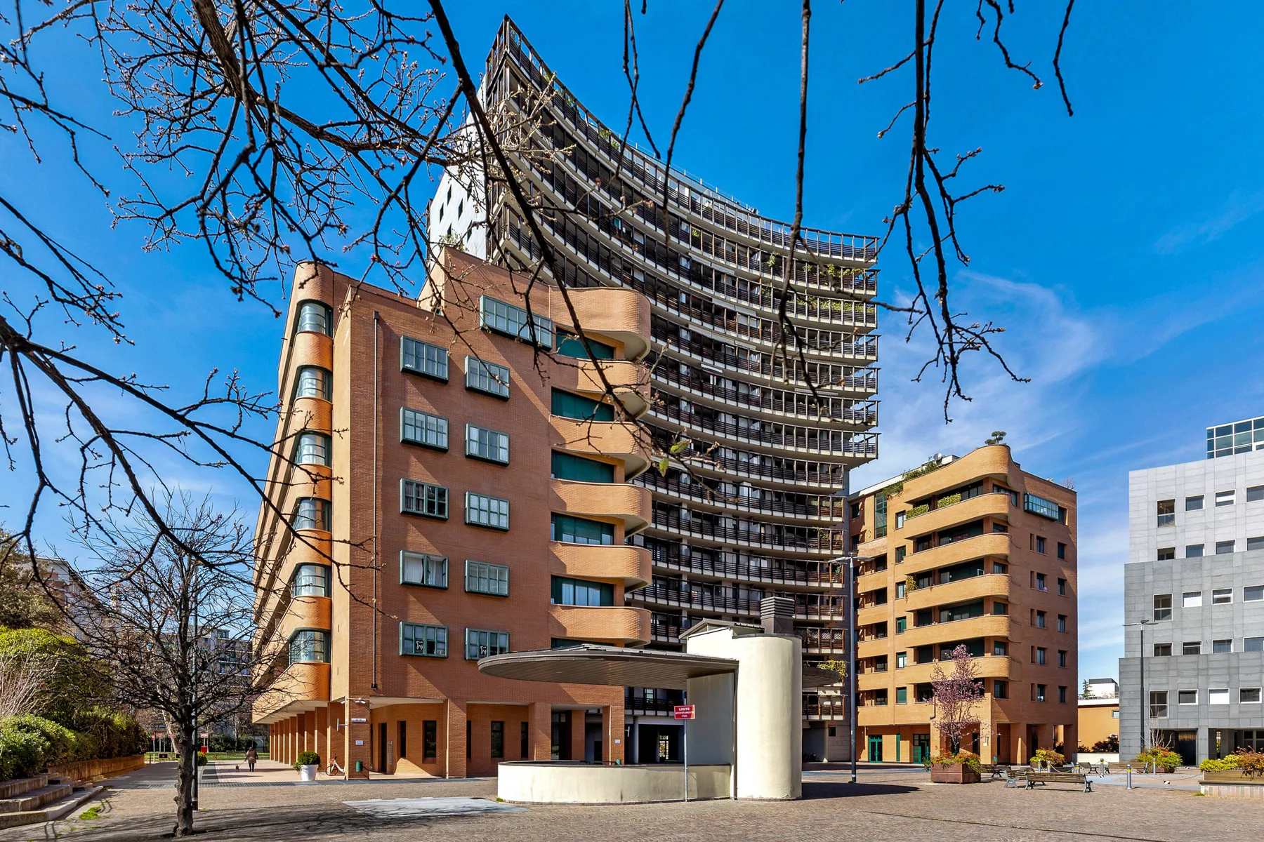 Edificios urbanos modernos bordean una plaza pavimentada bajo un cielo azul despejado.