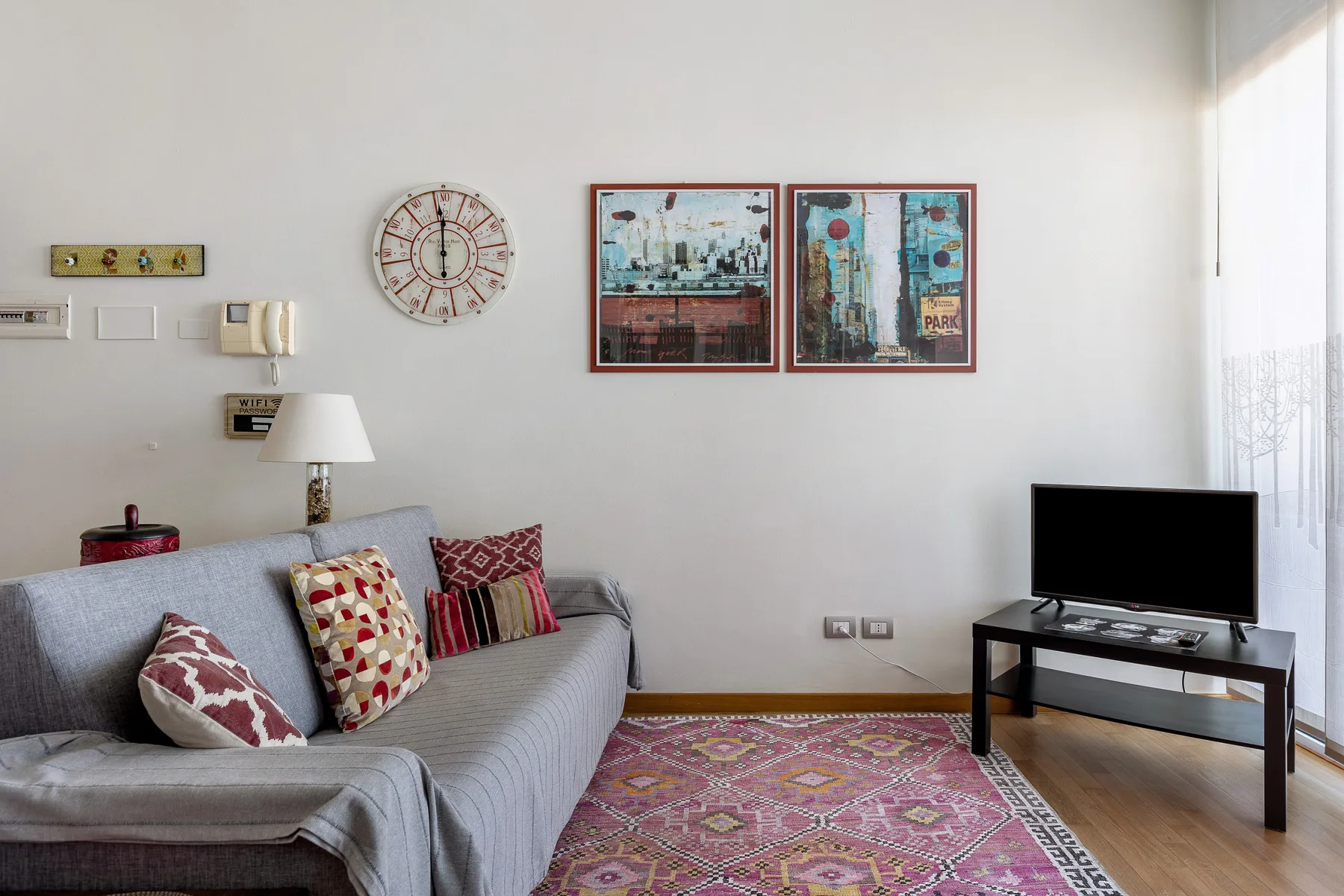 Una sala de estar con un sofá gris, cuadros coloridos y una alfombra estampada.