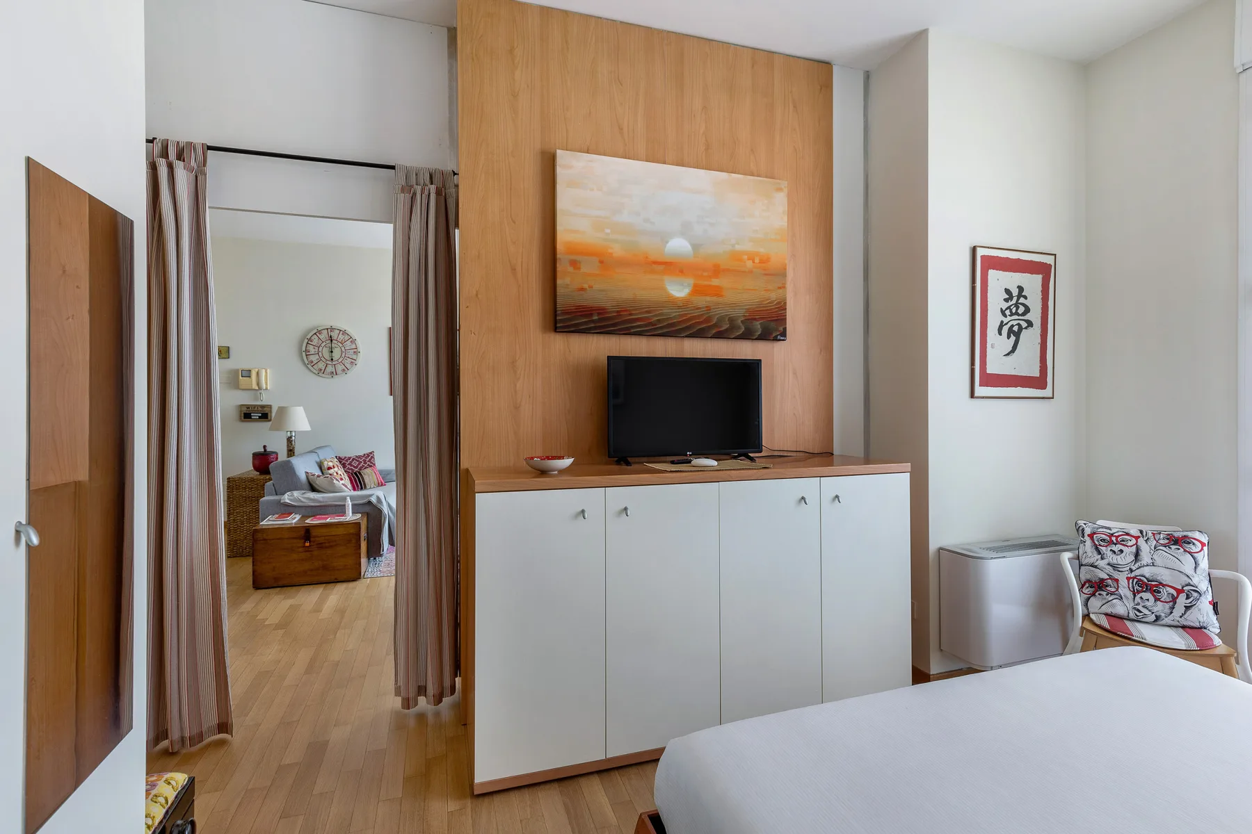 Un dormitorio con un televisor sobre un mueble y una cama en primer plano.