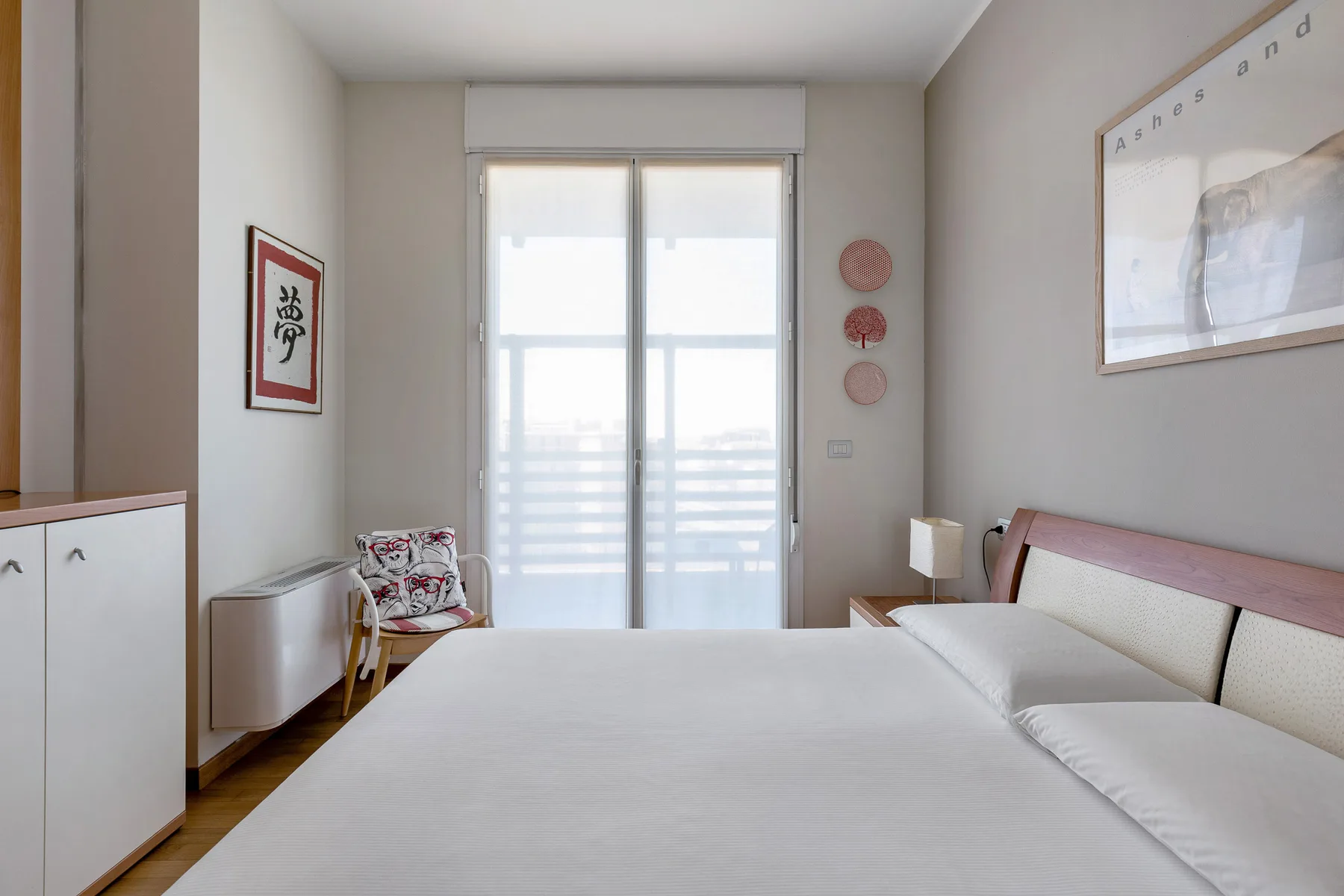 Un dormitorio luminoso con una cama bien tendida y puertas de vidrio que dan a un balcón.