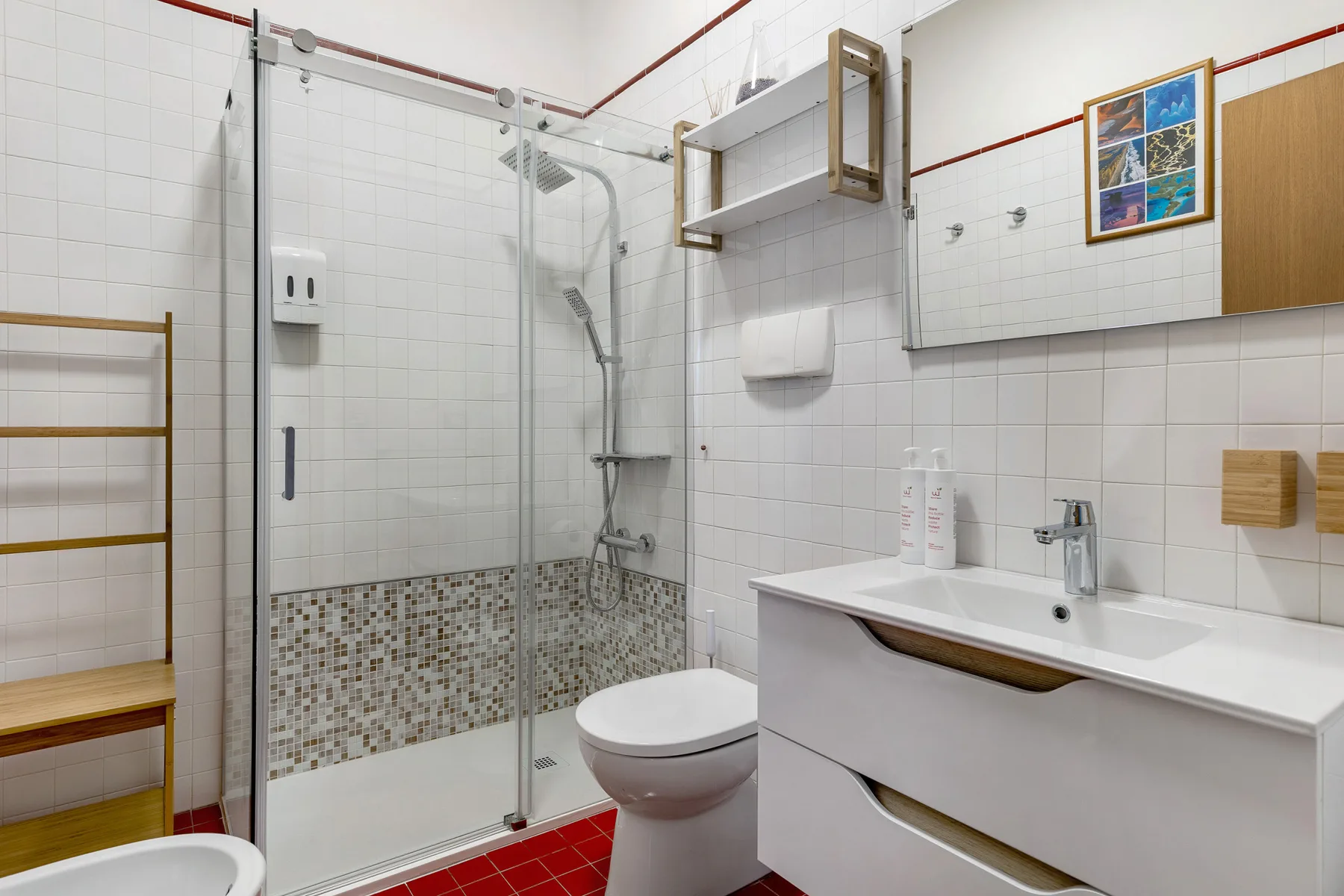 Un baño con azulejos, ducha de vidrio, lavabo y espejo en la pared.