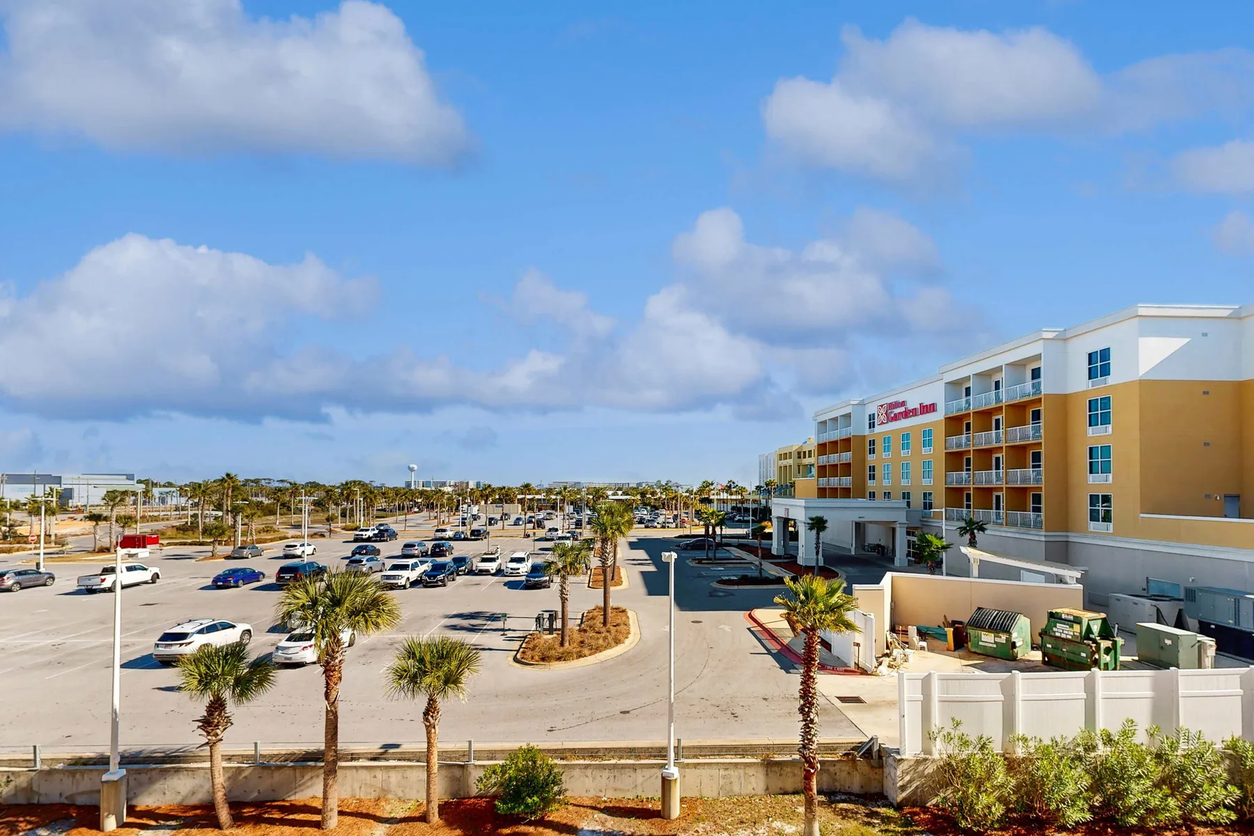 A commercial building overlooks a parking lot lined with palm trees.