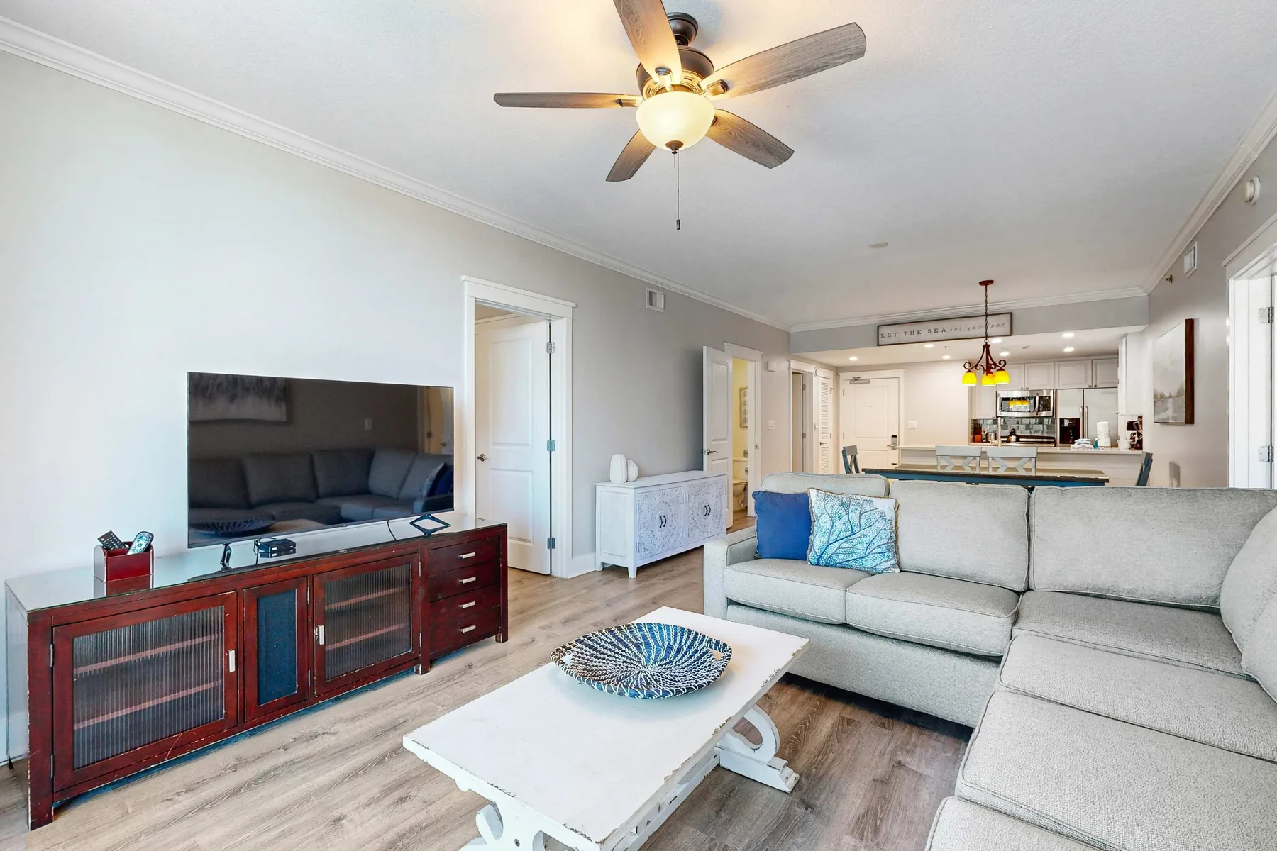 A living room with seating, a television, and an open kitchen beyond.