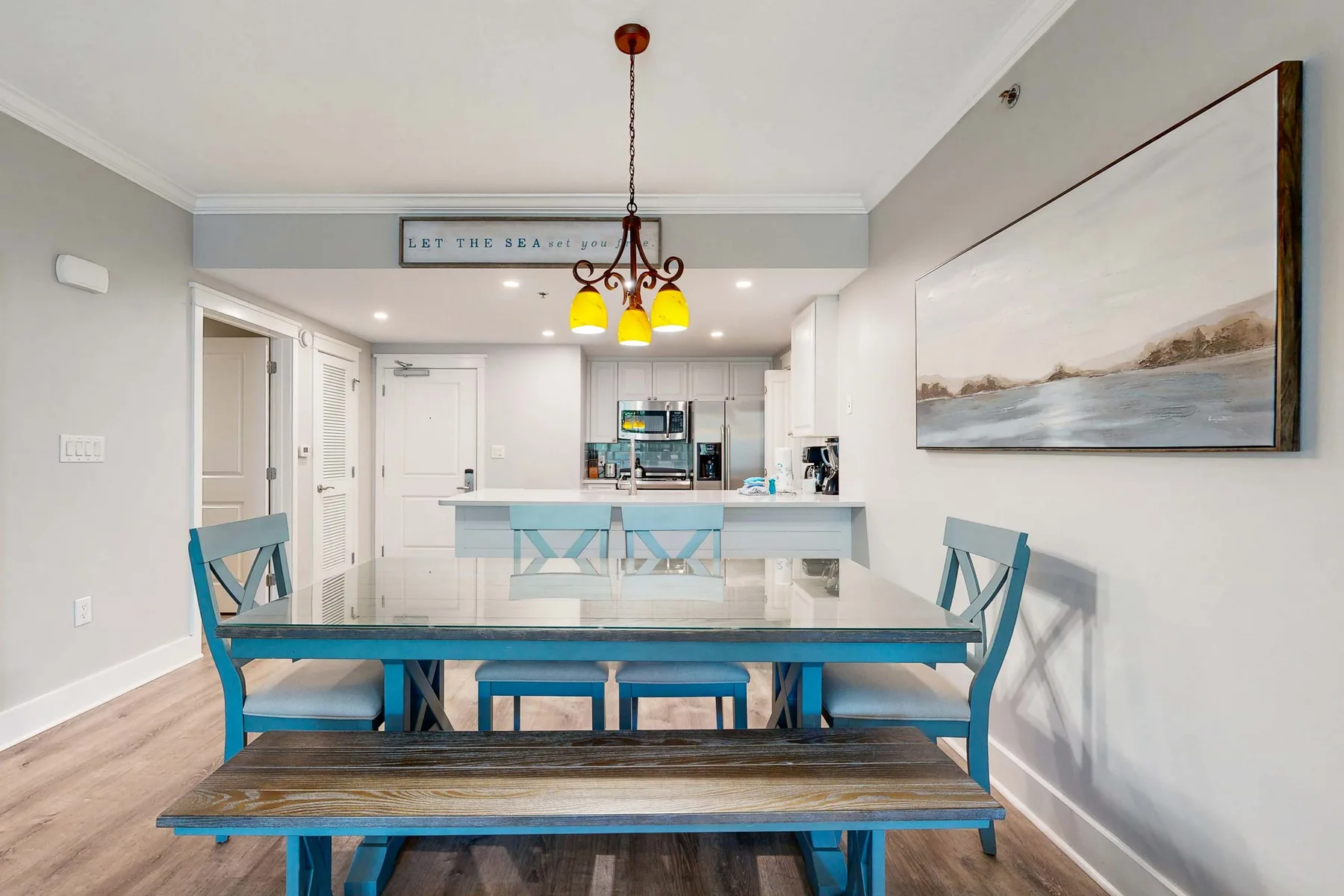 A dining area with a table and blue seating faces an open kitchen.