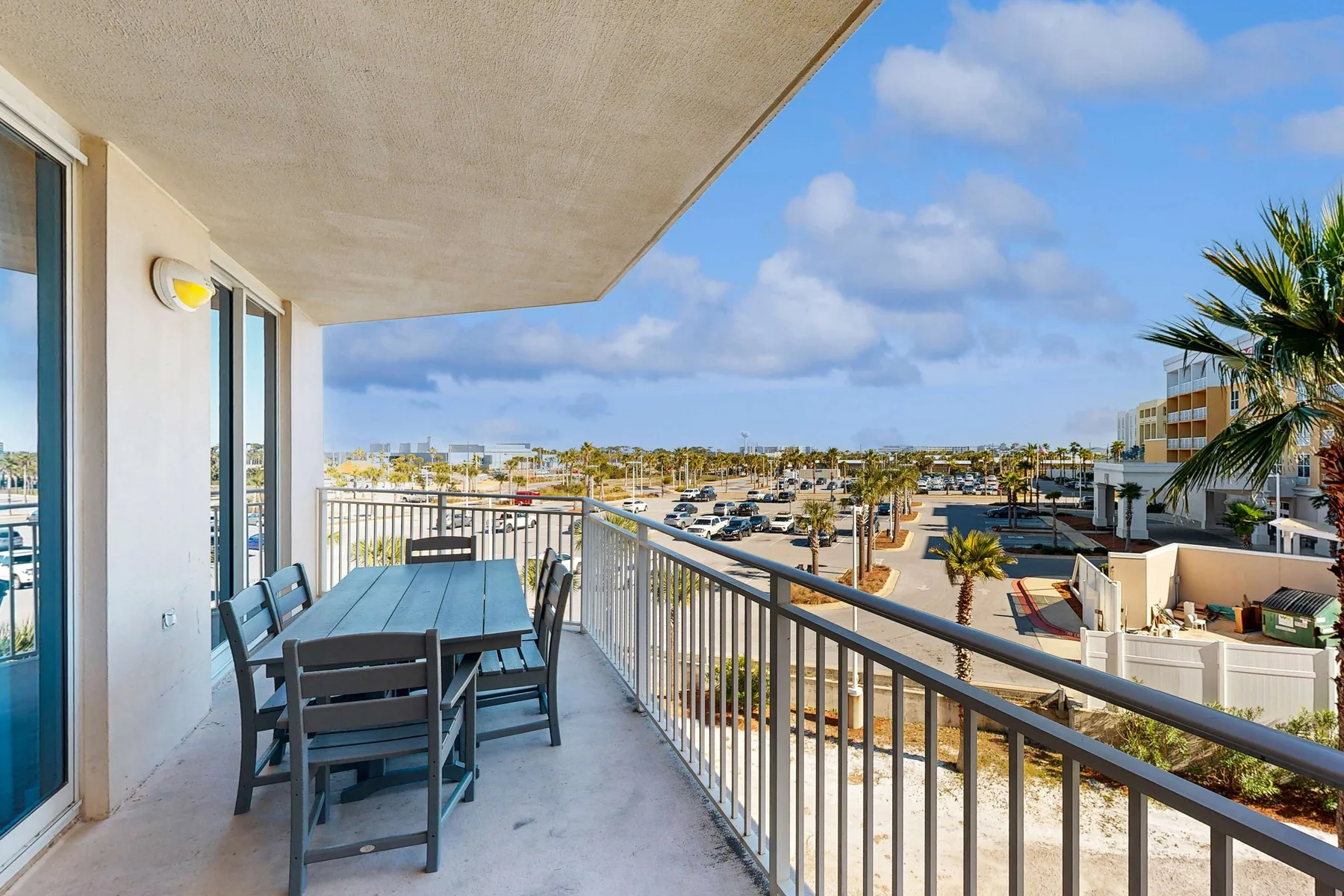 A balcony seating area overlooks nearby buildings and a parking lot under a partly cloudy sky.