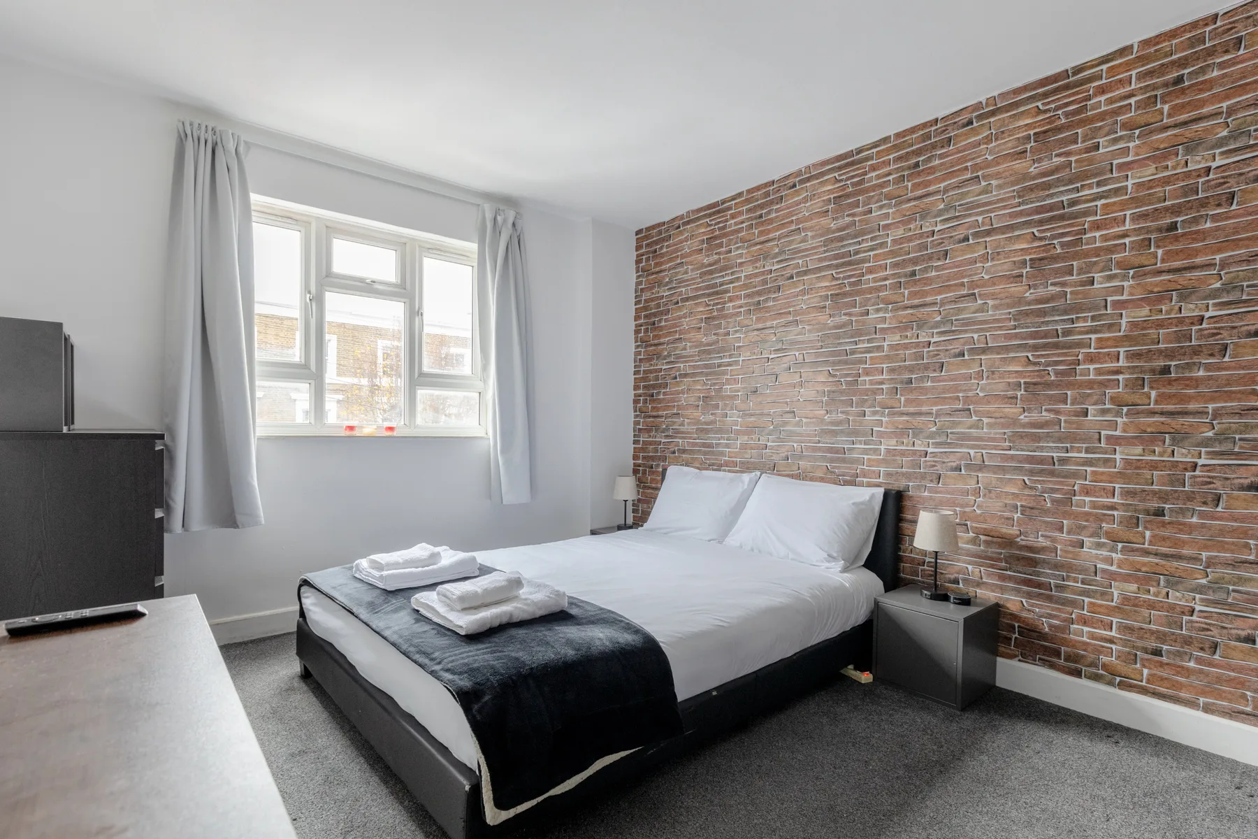 A bedroom with a bed, a brick wall, and a window.