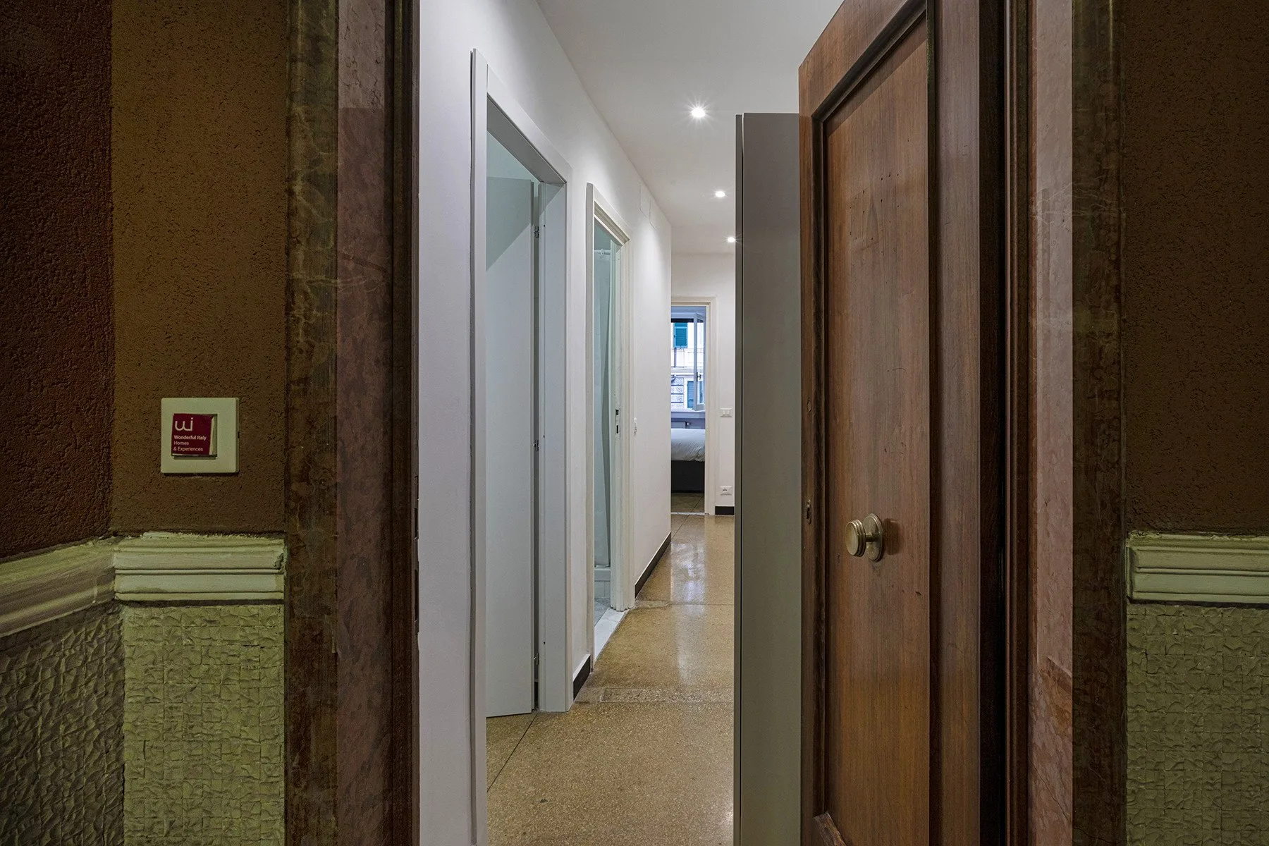 Un pasillo estrecho con puertas de madera y vista a una habitación luminosa.